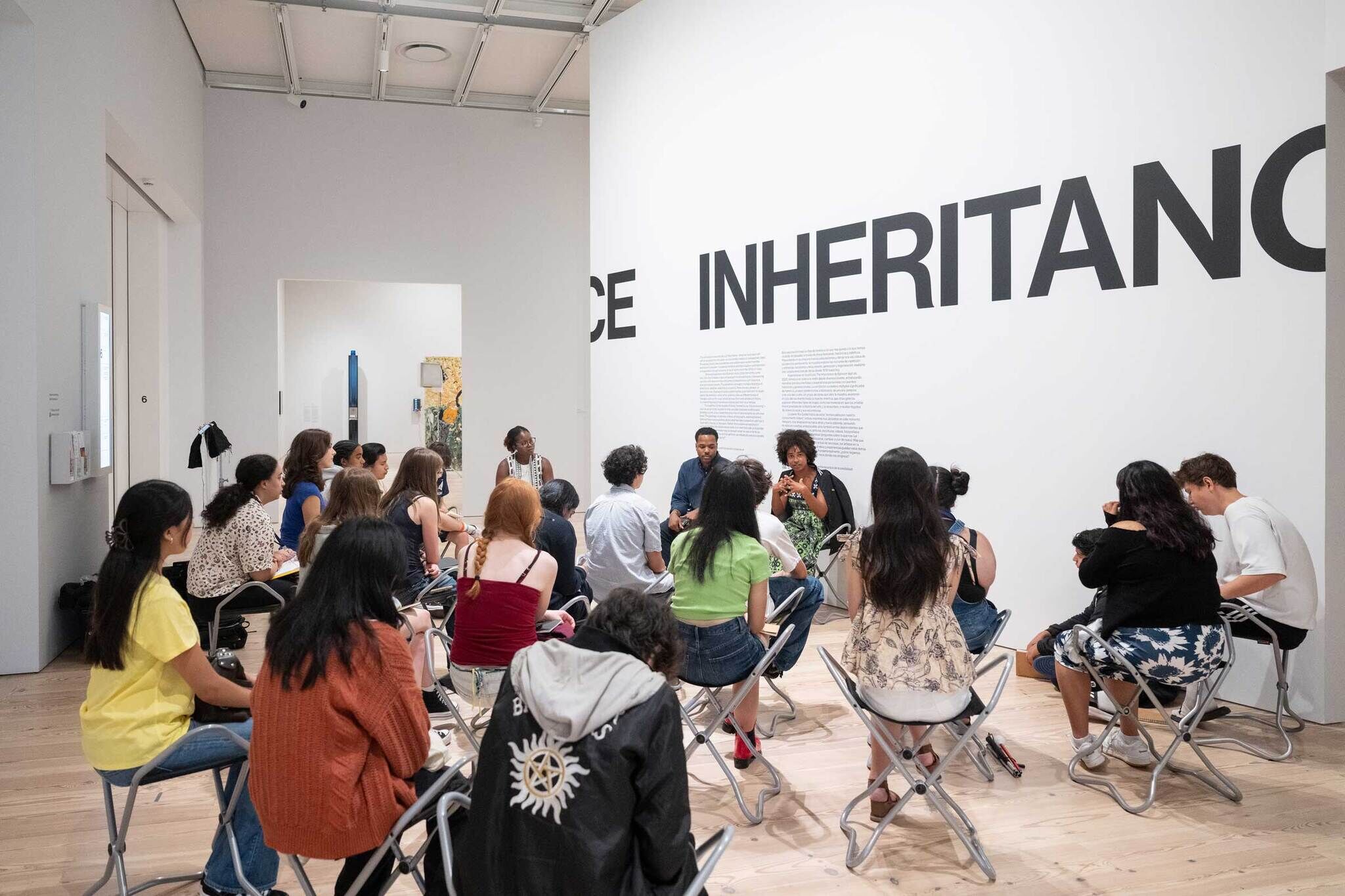 A bunch of youths sitting on chairs listening to two adults in front of a wall with text that says "Inheritance."
