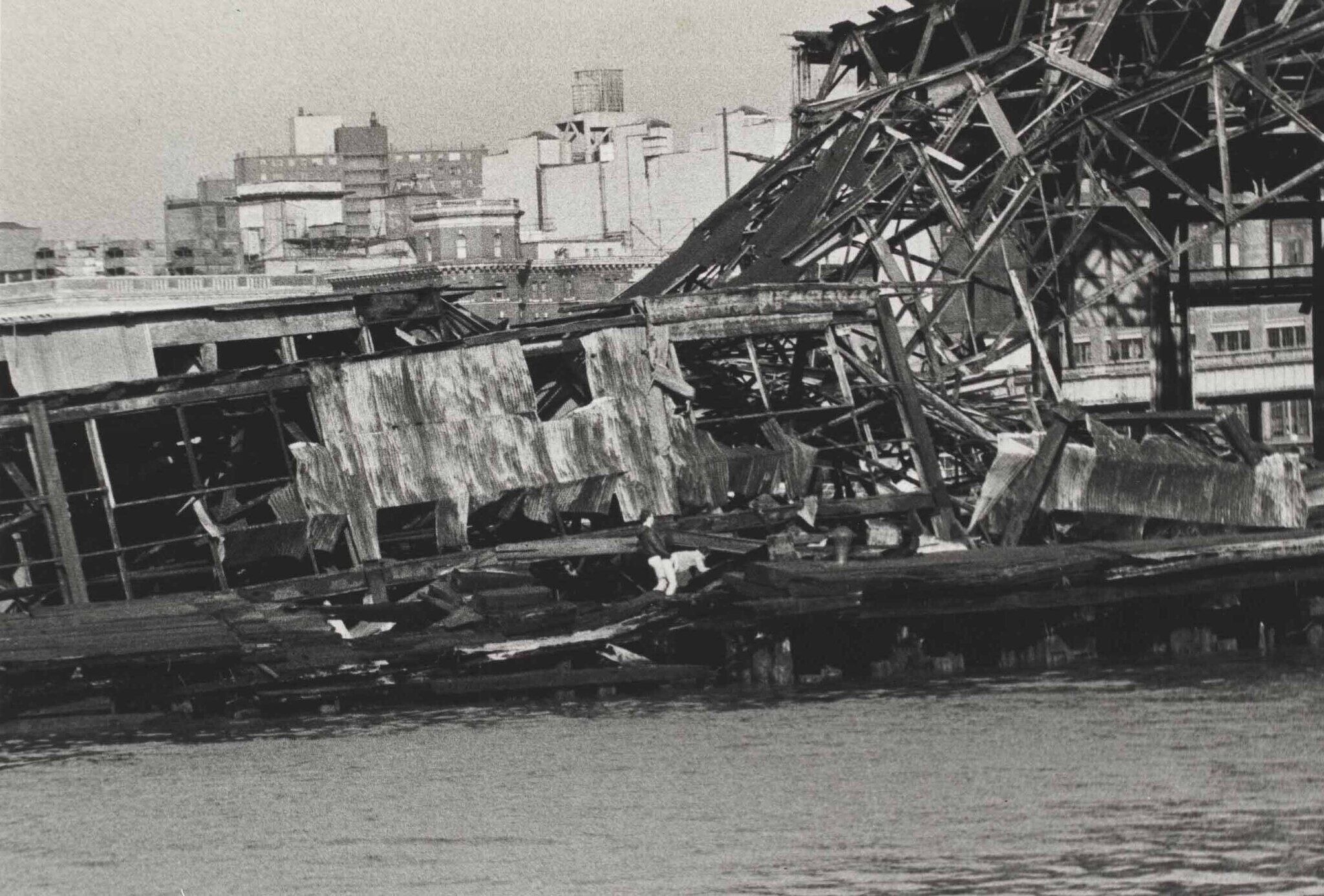 A black and white photograph of a collapsed building on the pier, two men are fornicating in the middle.