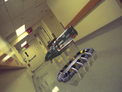 Computer generated industrial looking metal shapes sit in the middle of a photo of a hospital hallway at a dutch angle.