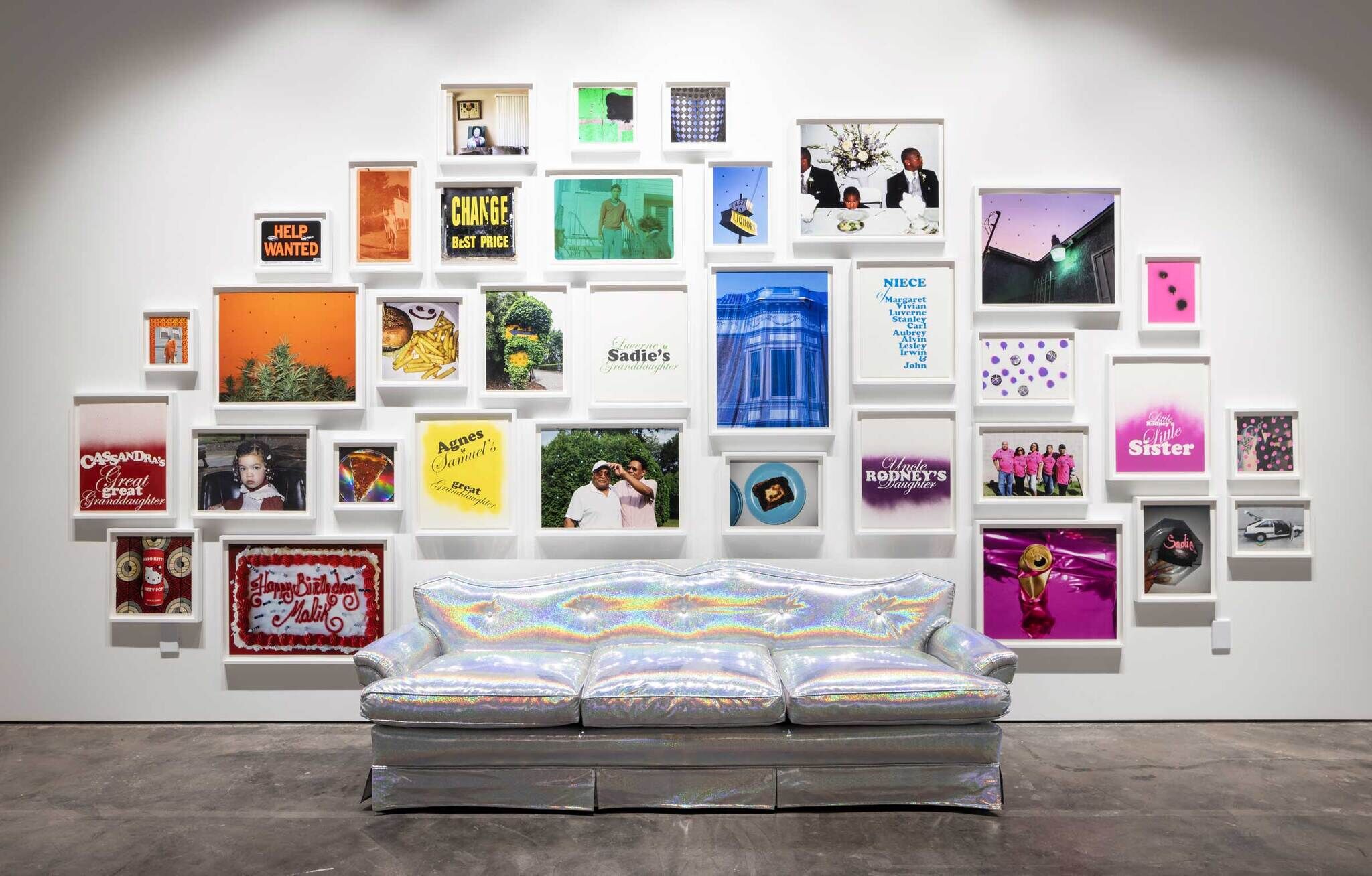 A couch upholstered in iridescent vinyl sits in front of a wall of colorful framed photographs and posters arranged in the chromatic order of a rainbow. 