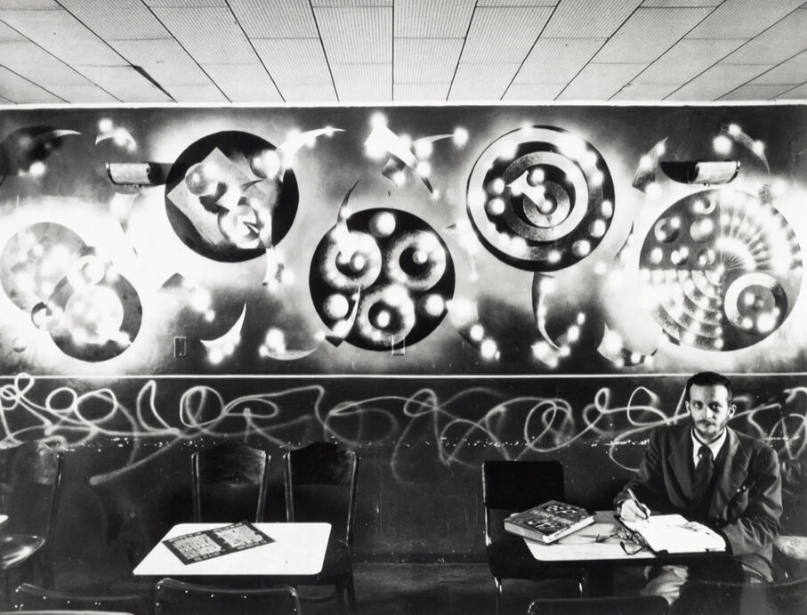 A person sits in front of a mural with swirling shapes at a restaurant. 