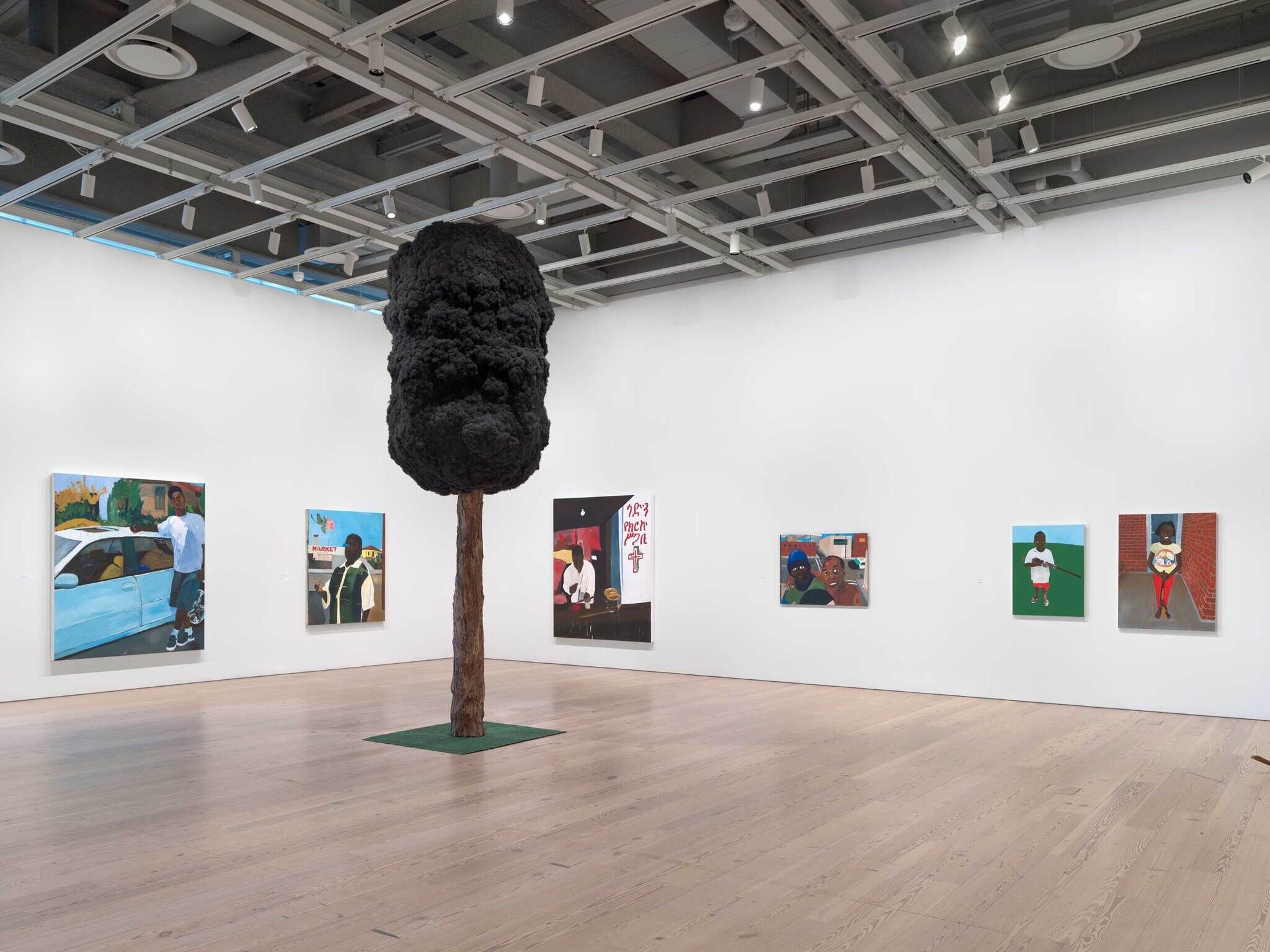 A large sculpture of a tree with hair-like leaves in front of multiple painted portraits.