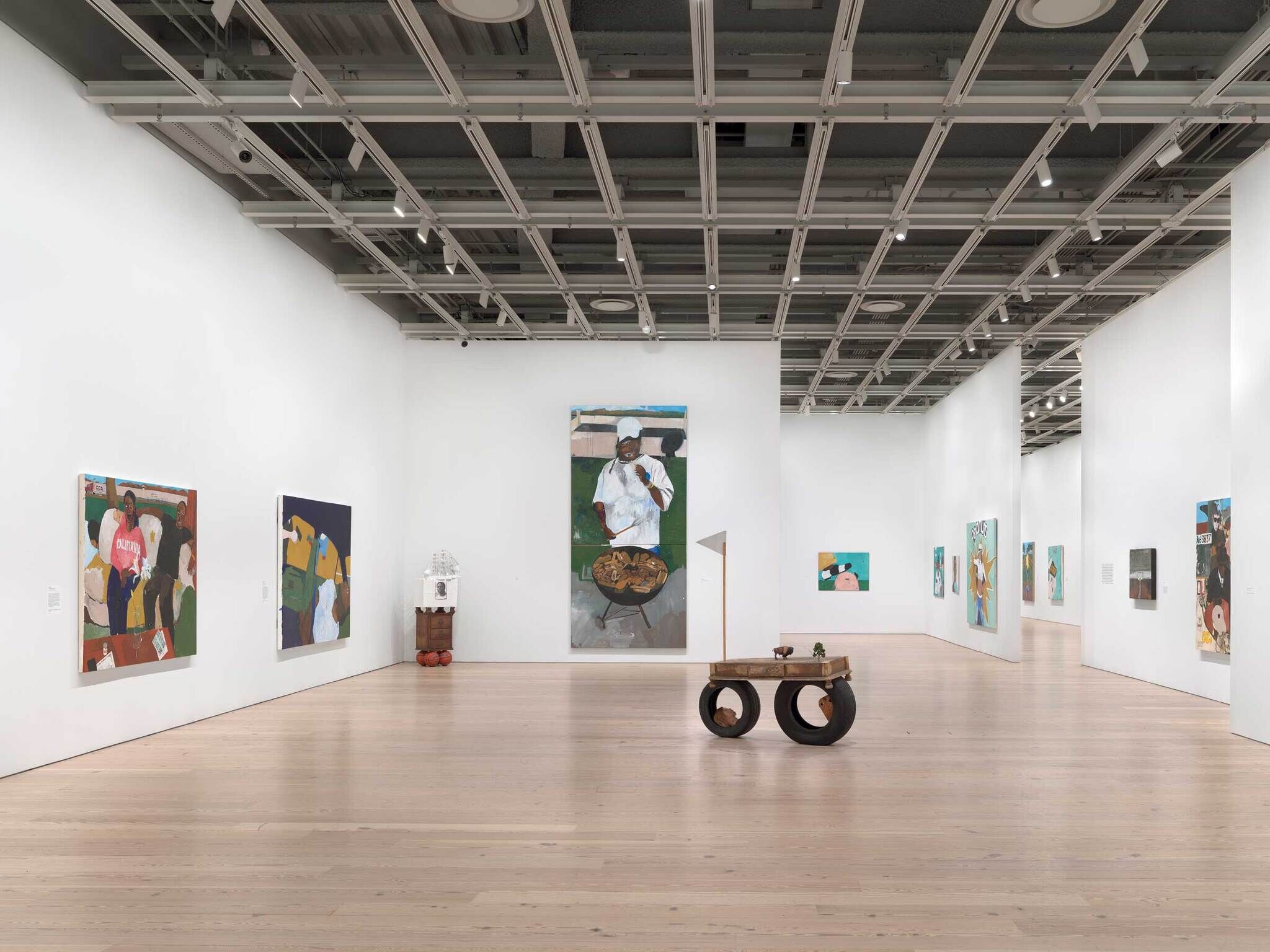 Multiple rooms with 11 paintings of portraits total, a sculpture of a cabinet on top of two basketballs in the left corner, and a sculpture of a bison on top of two tires with a white flag in the foreground.