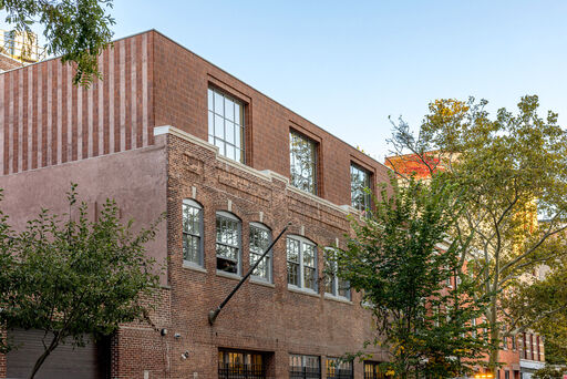 A three-floor brick building with leafy trees in front. 