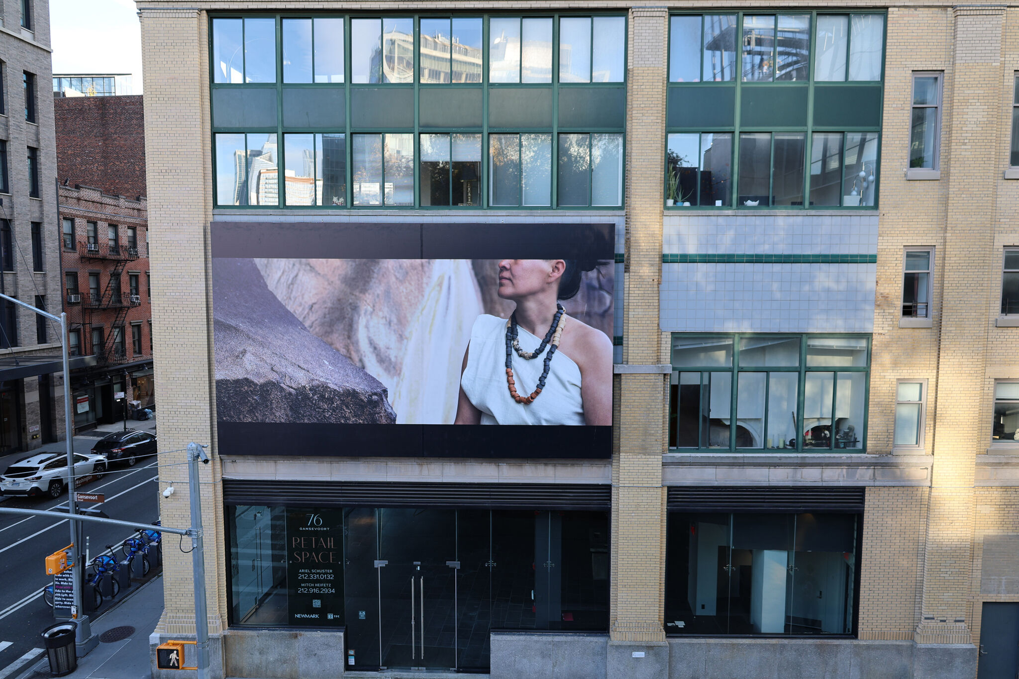 A billboard above a busy street with a photograph of a woman wearing a necklace and stone textures behind. 