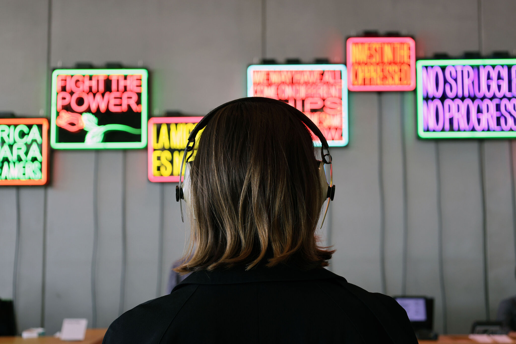 A person wearing headphones standing in front of a neon sculpture. 