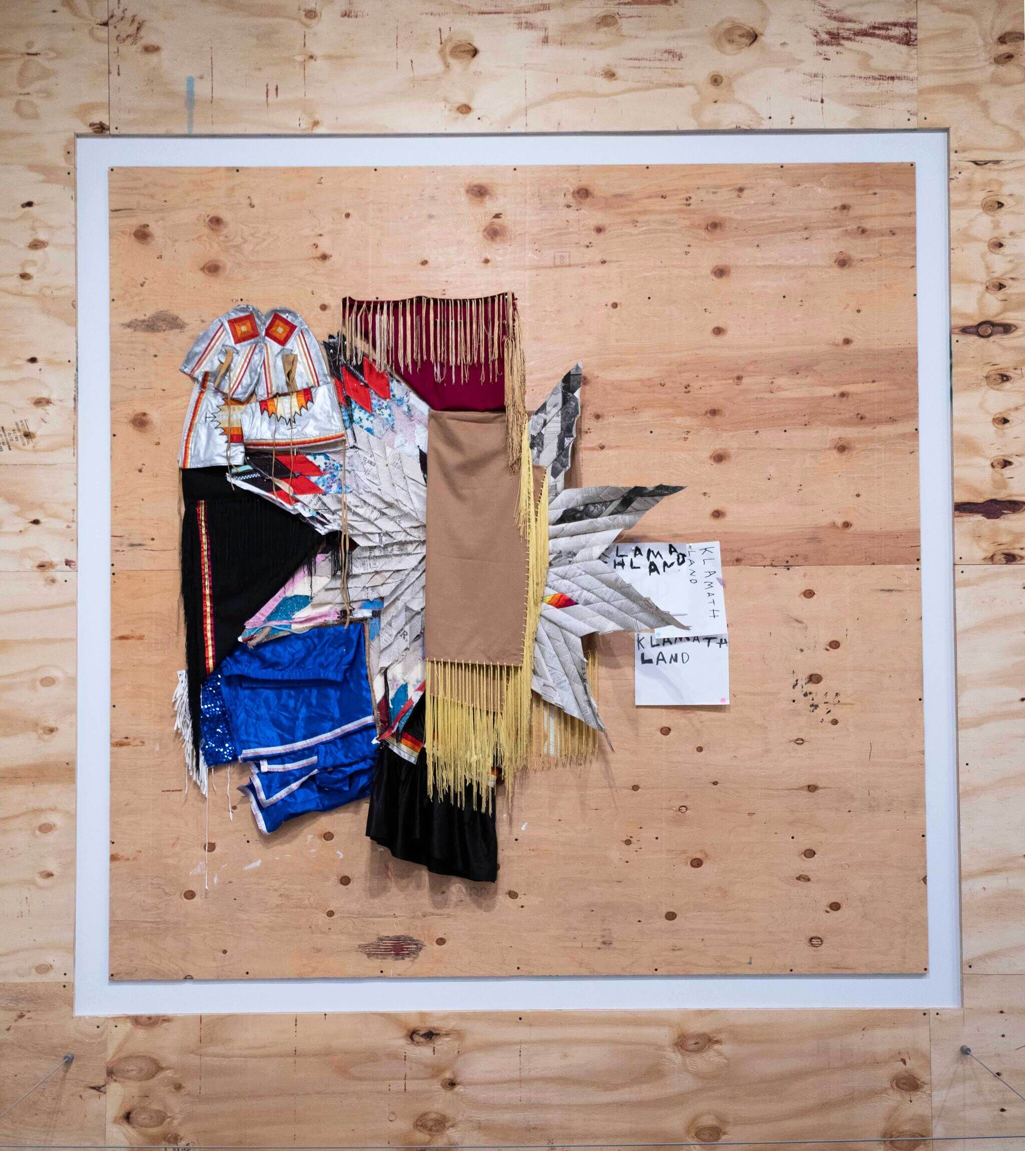 A collage of different materials like fabrics and star quilts and sequins on a light wood wall.