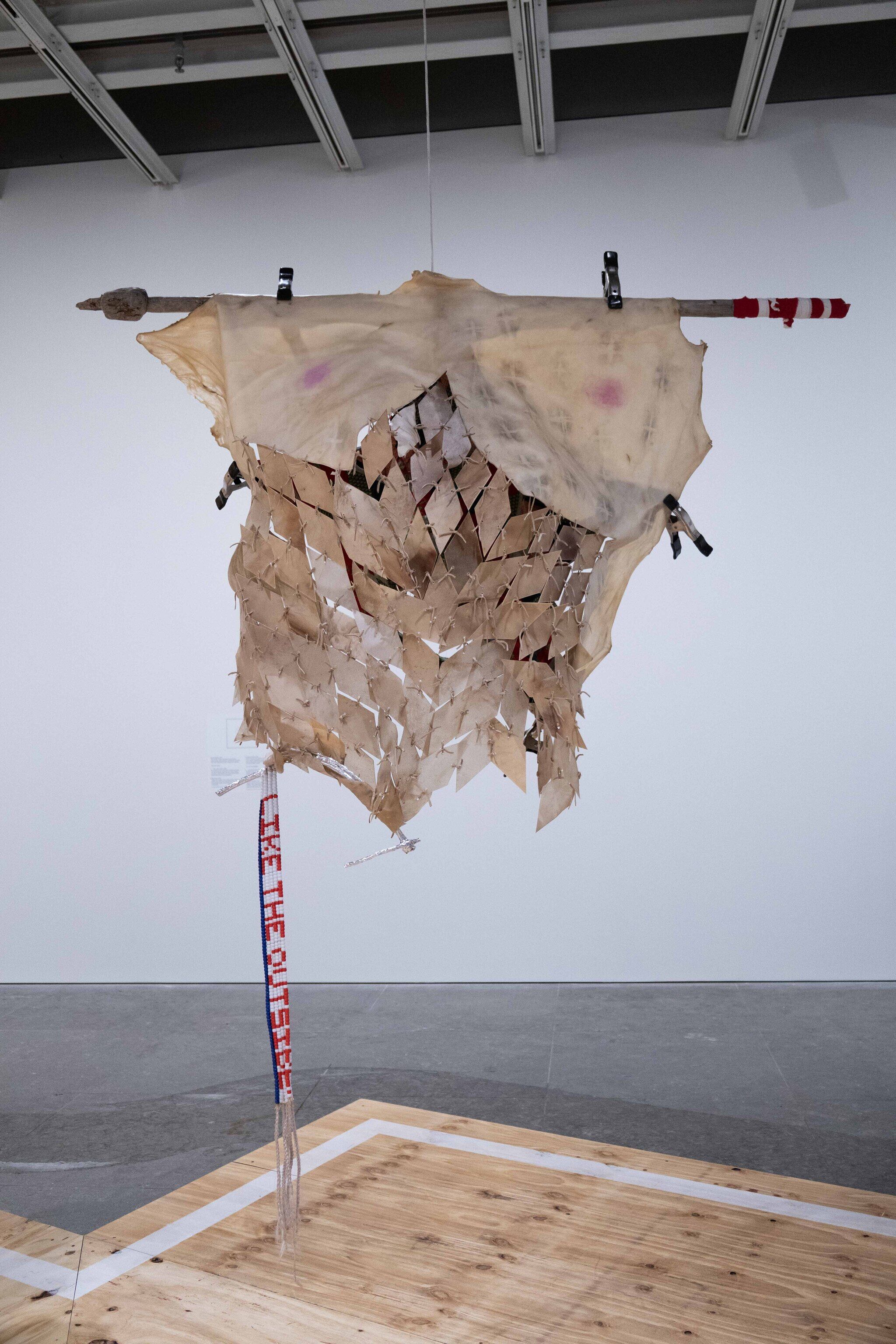 This work features a hanging assemblage of elk rawhide, cotton, newspaper, wood, leather, plastic beads, willow branches, artificial hair, aluminum foil, chalk, metal clamps, rope, makeup, and graphite, suspended in the air. 