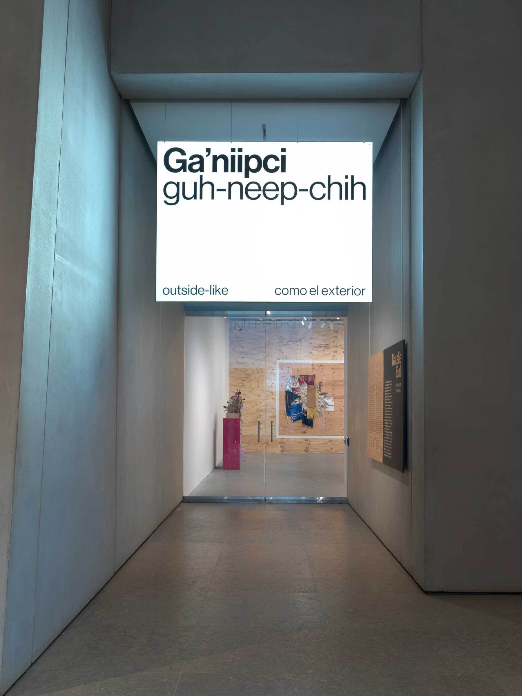A museum corridor with a sign overhead displaying words in three languages, leading to an exhibition space.