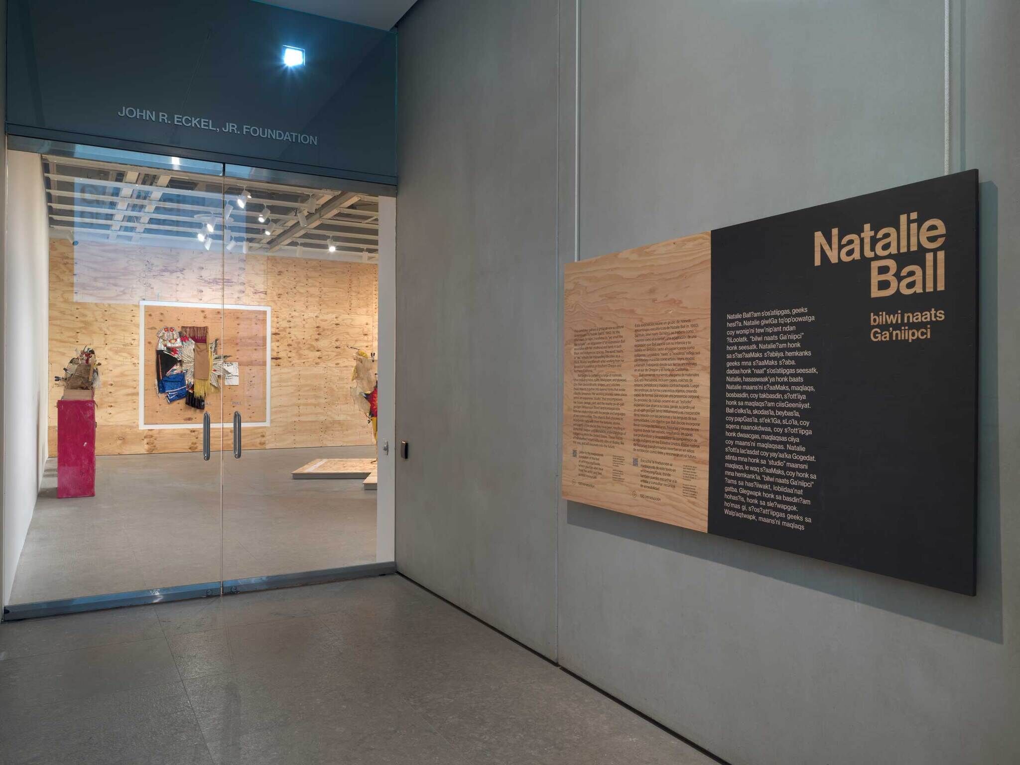 Entrance to an art gallery with "Natalie Ball" exhibition text on the wall and artwork visible through glass doors.