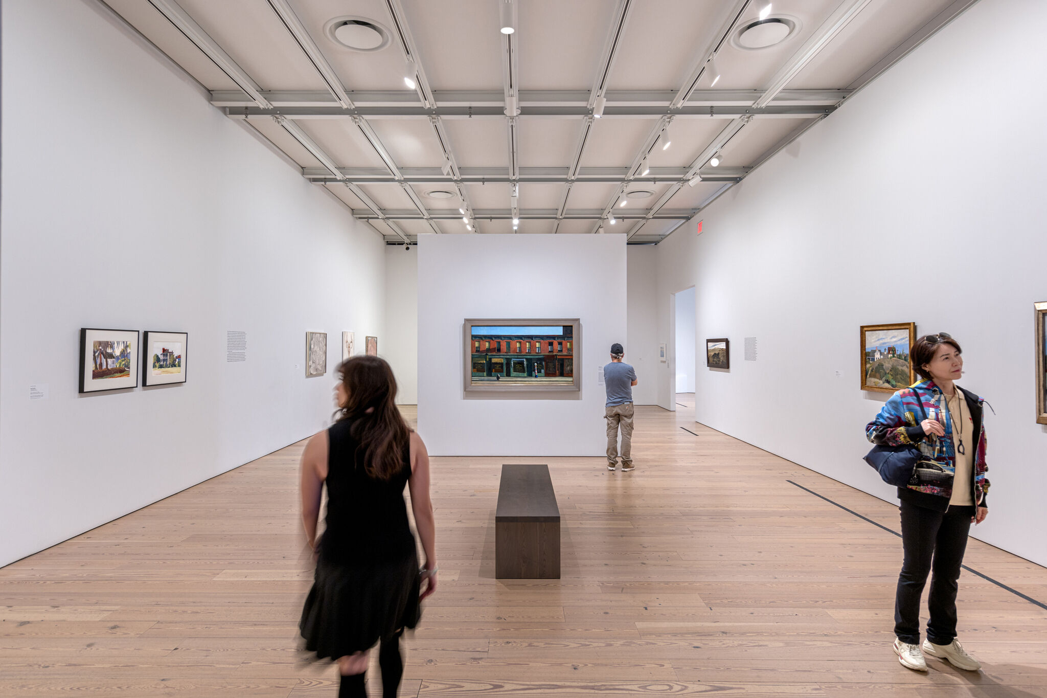 Visitors viewing artwork in a modern gallery with wooden floors and white walls.