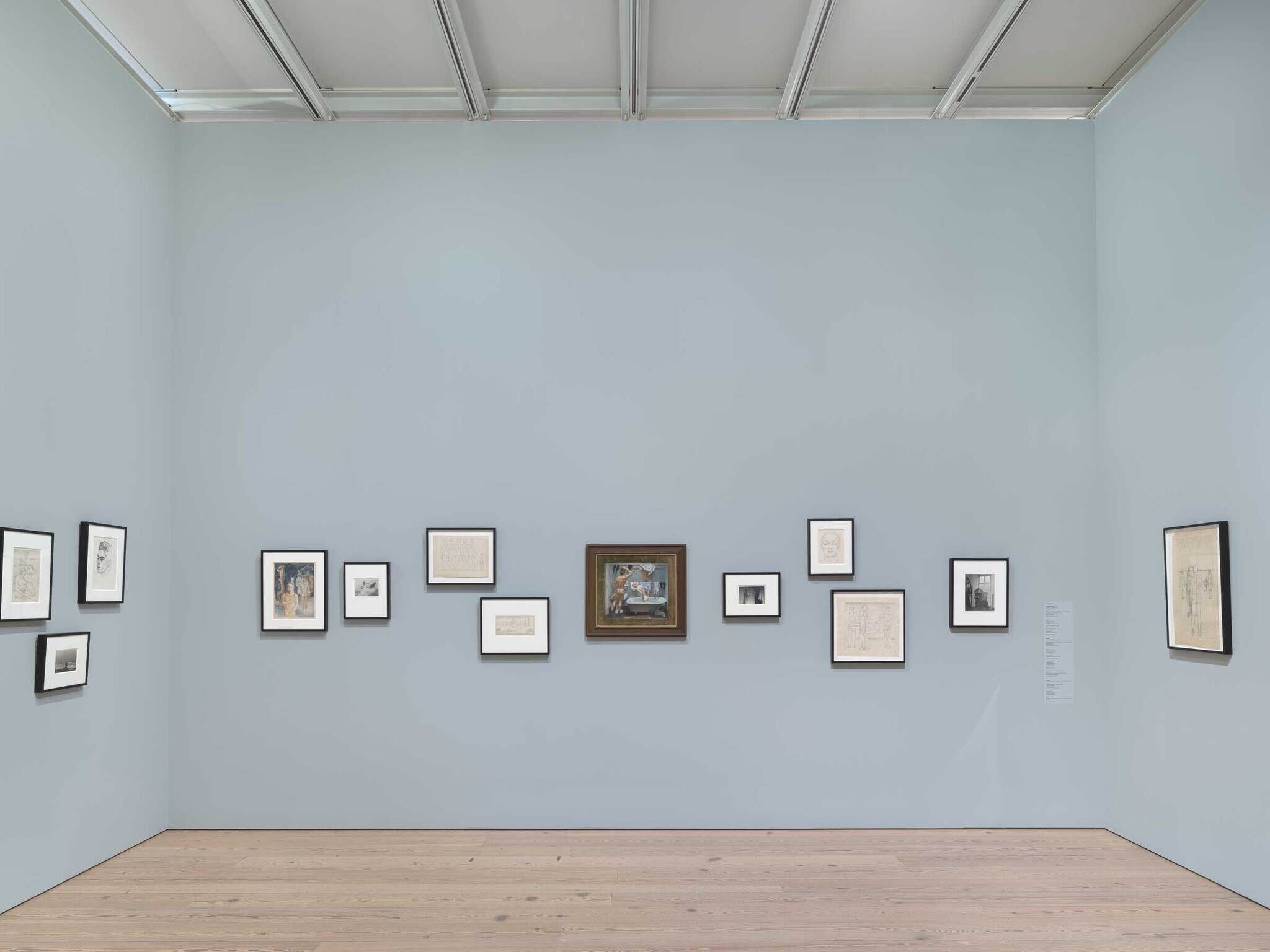 Art gallery interior with various framed artworks on a light blue wall and wooden flooring.