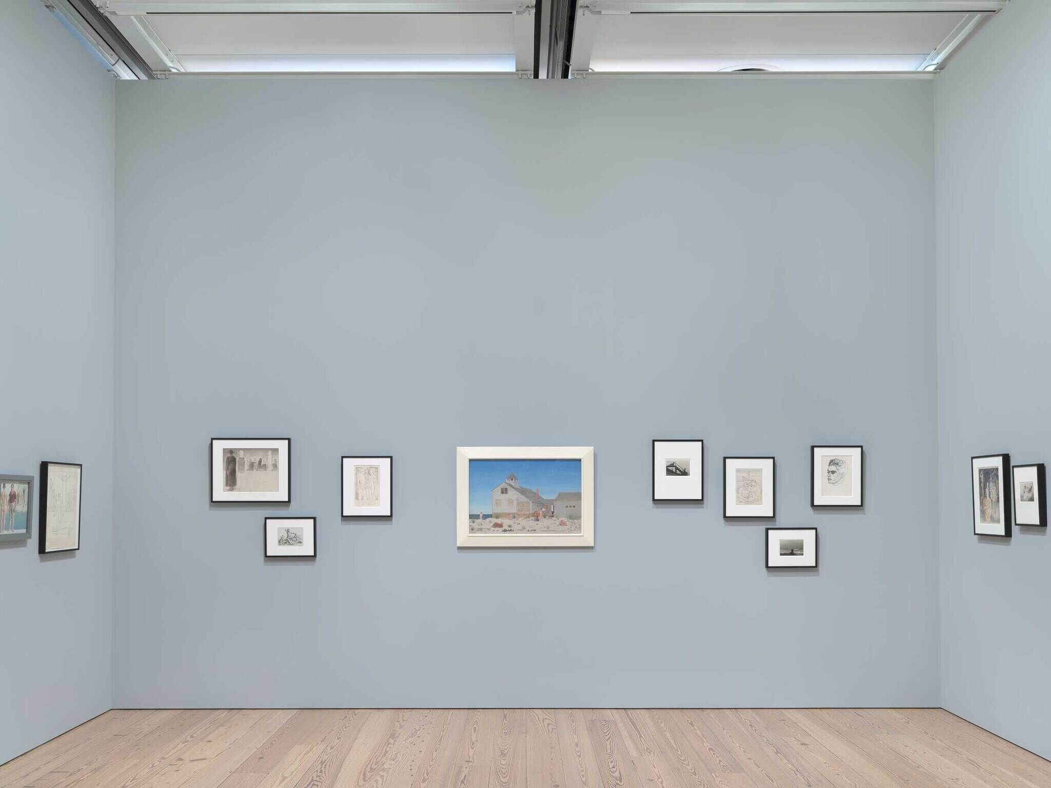 Art gallery interior with framed artworks on a light blue wall and wooden flooring.