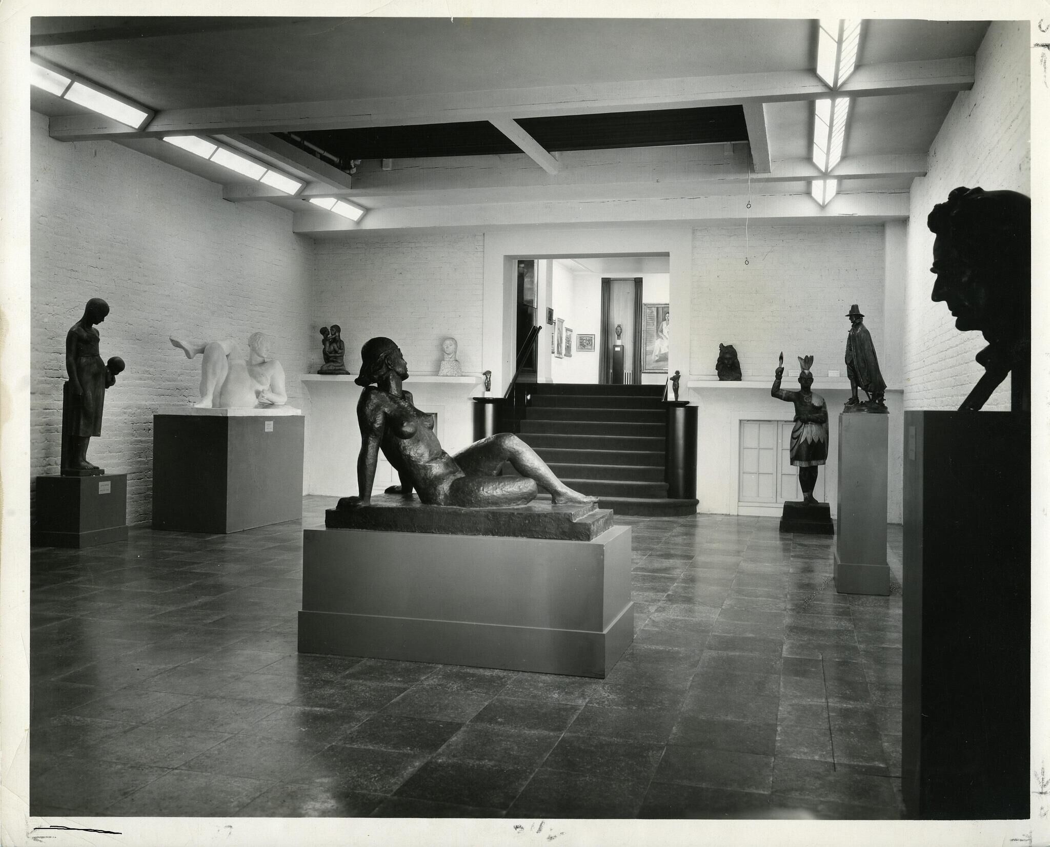 Interior of an art gallery with various sculptures on display, including a reclining figure in the foreground.