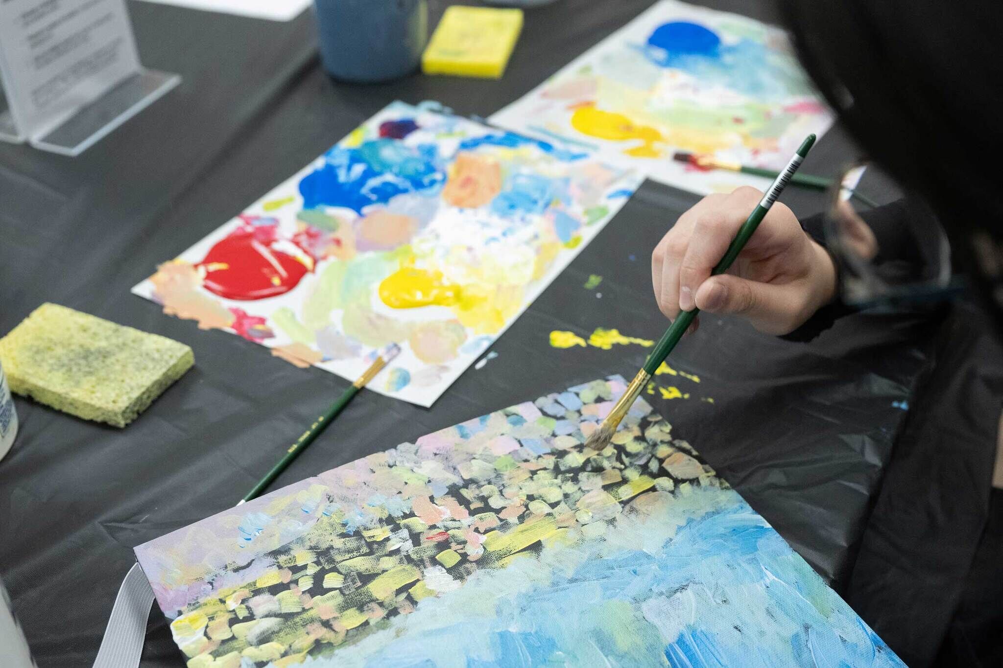 Teen paints with colorful, jagged, and uneven brushstrokes on a canvas board.