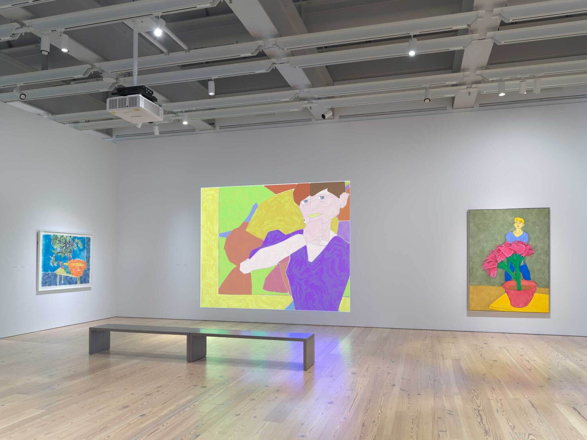 Modern art gallery interior with colorful abstract paintings on white walls, wooden floors, and a bench in the center.