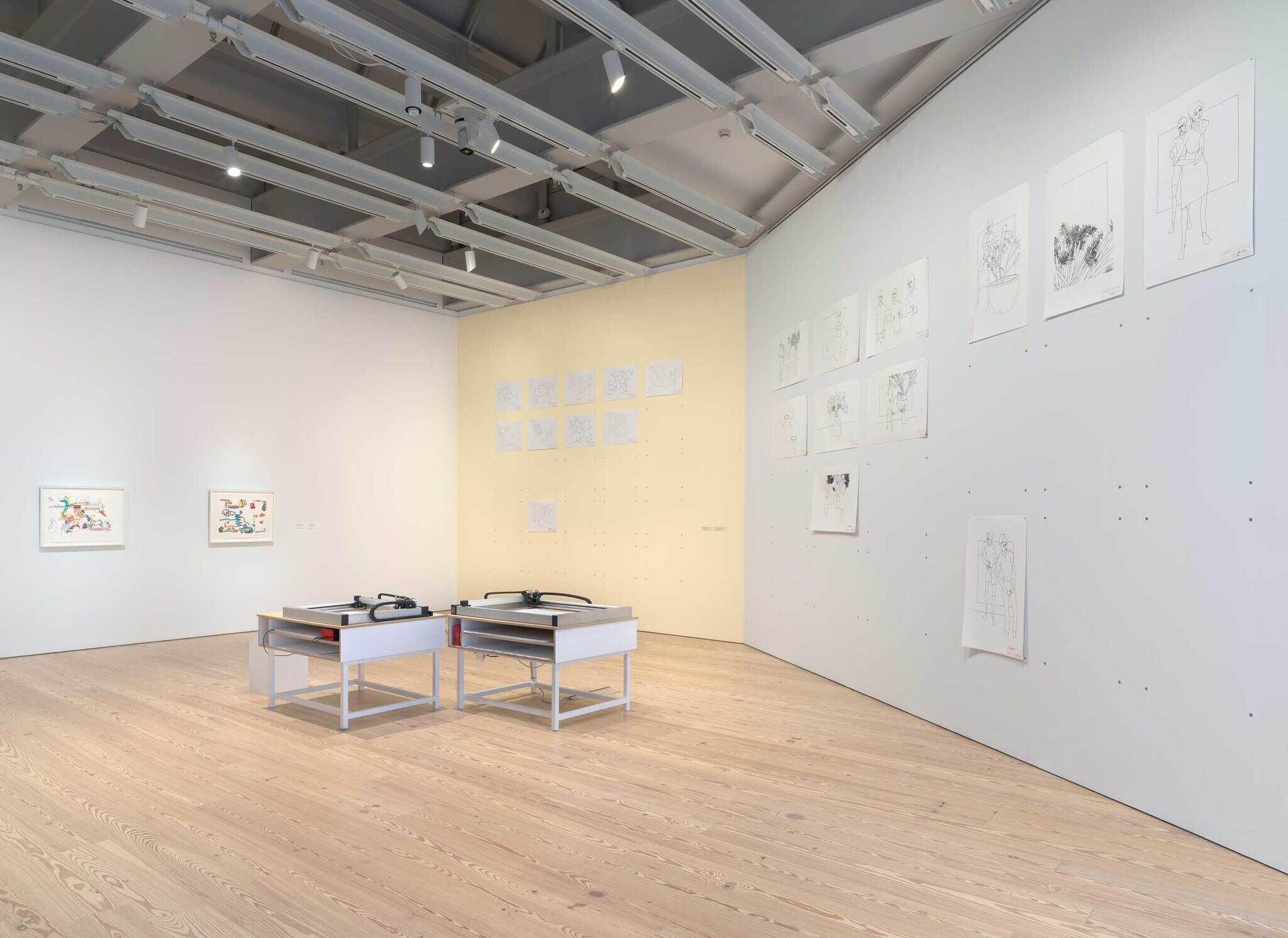 Modern art gallery interior with sketches on walls and two plotters drawing with a sharpie in the center.