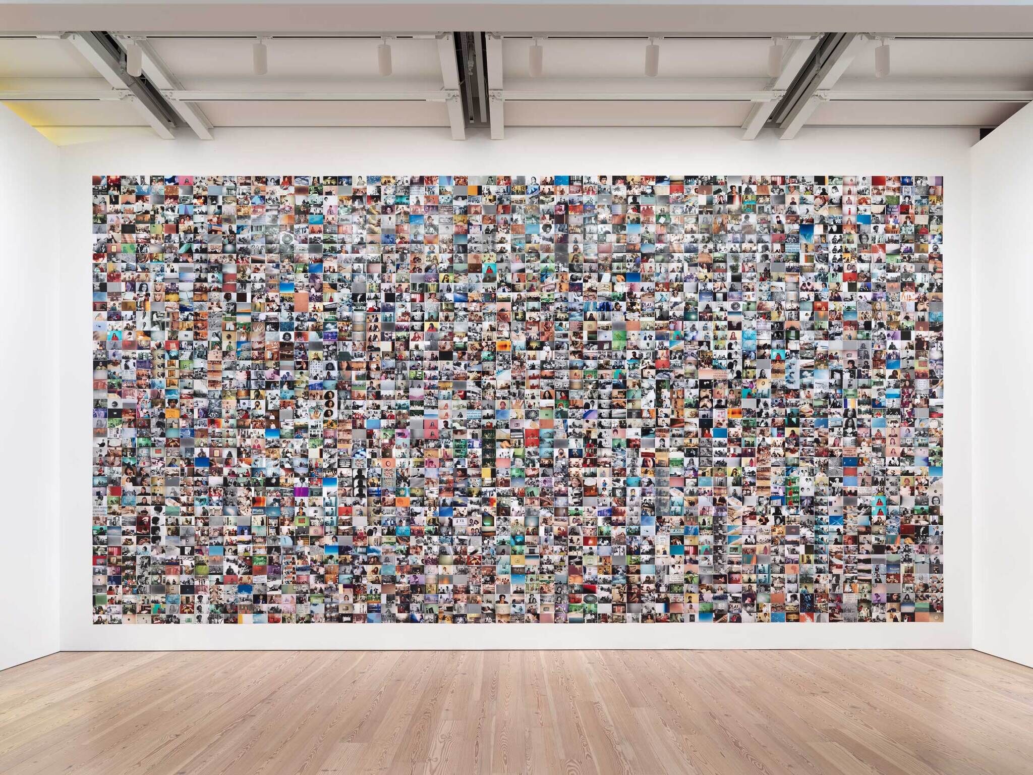 A large collage of numerous photos covering an entire gallery wall, viewed from a wooden floor.
