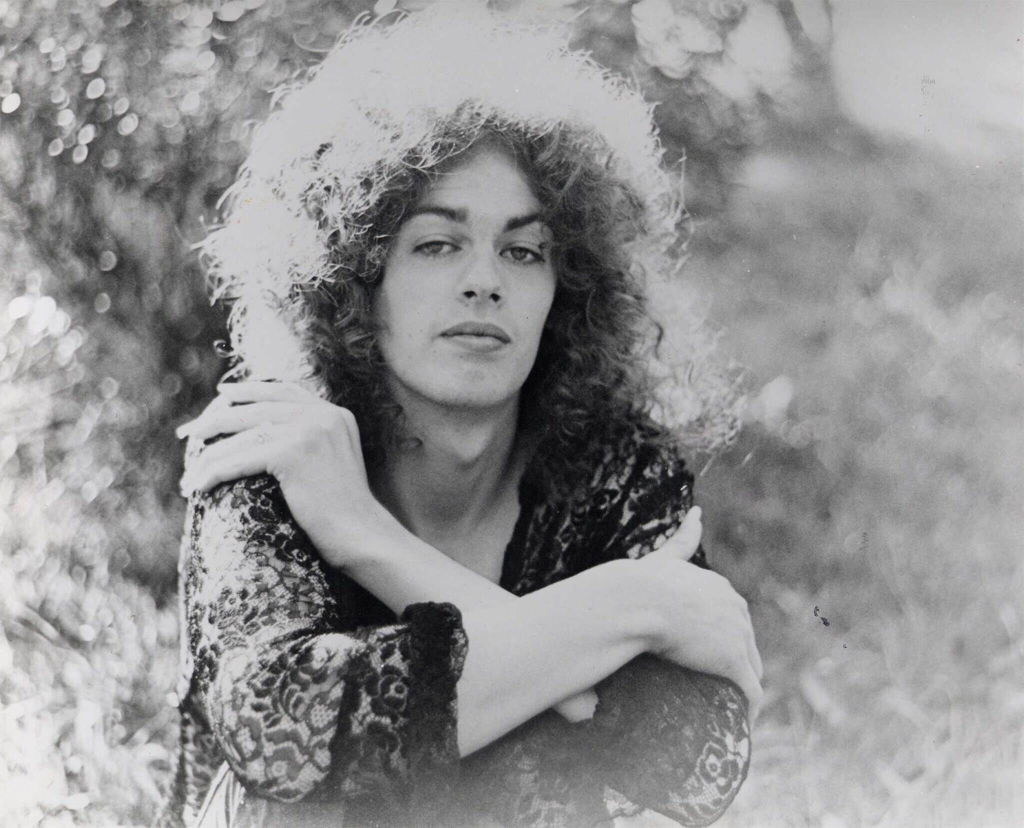 Black and white photo of a person with curly hair sitting outdoors, resting their chin on crossed arms.