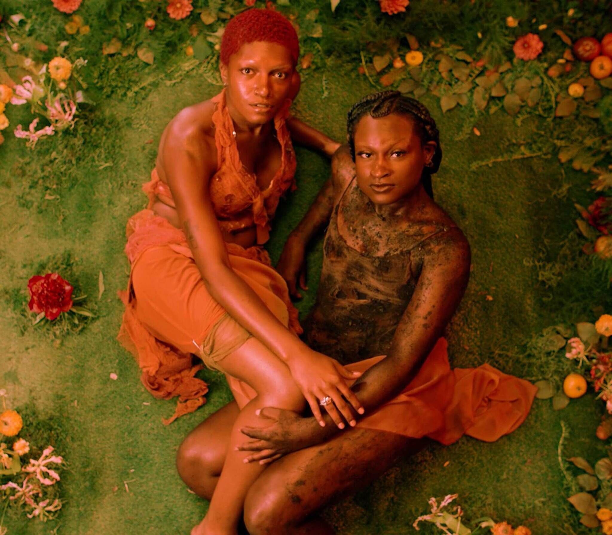 Two individuals with striking poses surrounded by lush greenery and vibrant flowers.