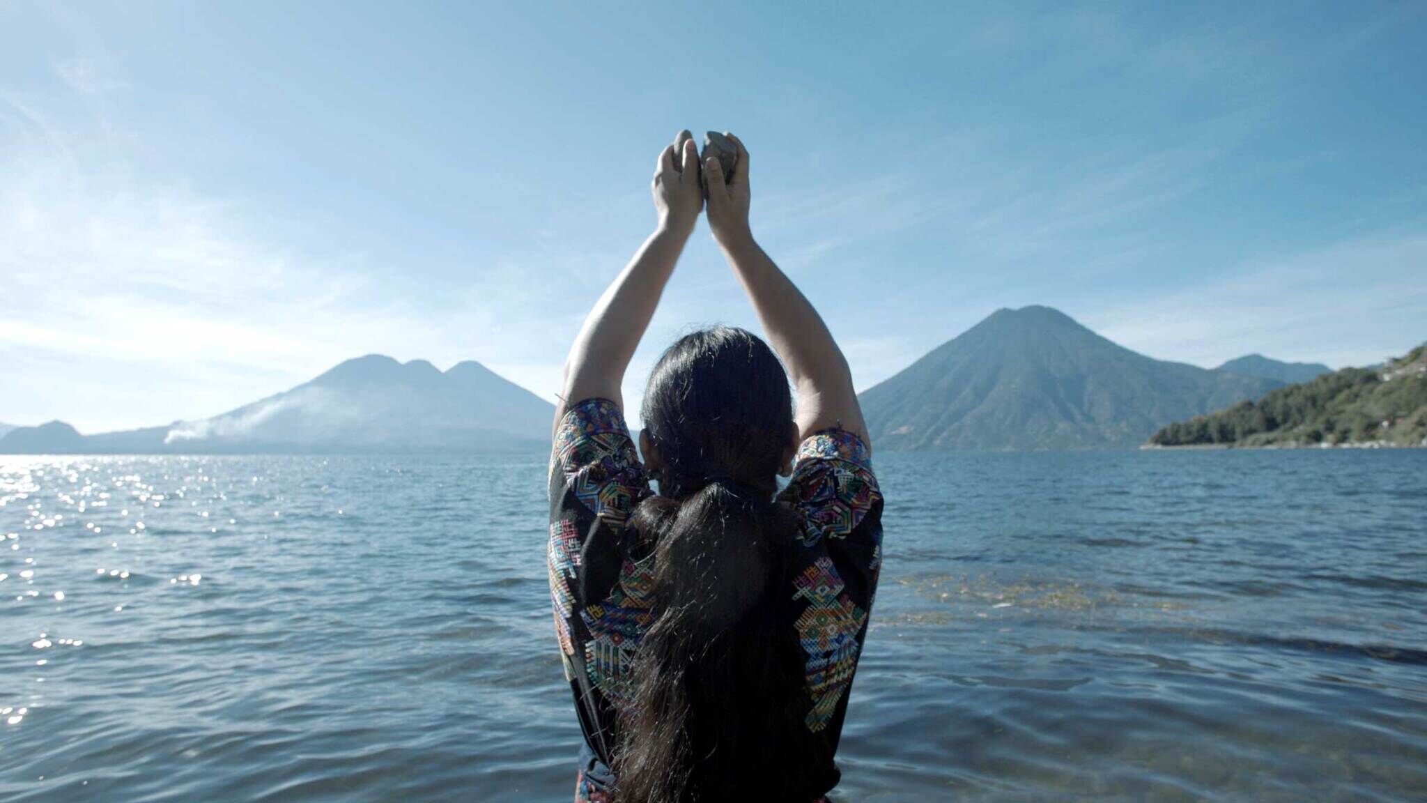 Person with arms raised facing a serene lake and mountains.