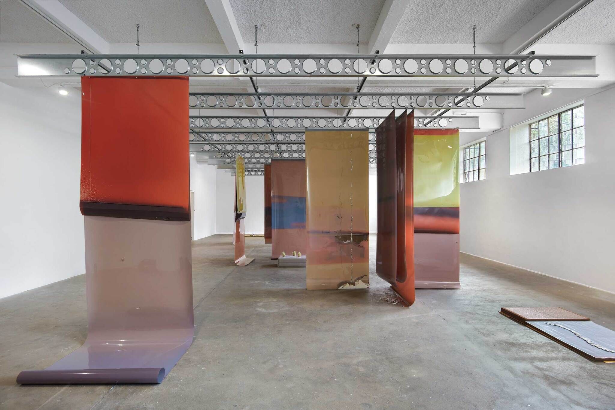 Modern art installation with large, colorful, semi-transparent sheets in an industrial gallery space.
