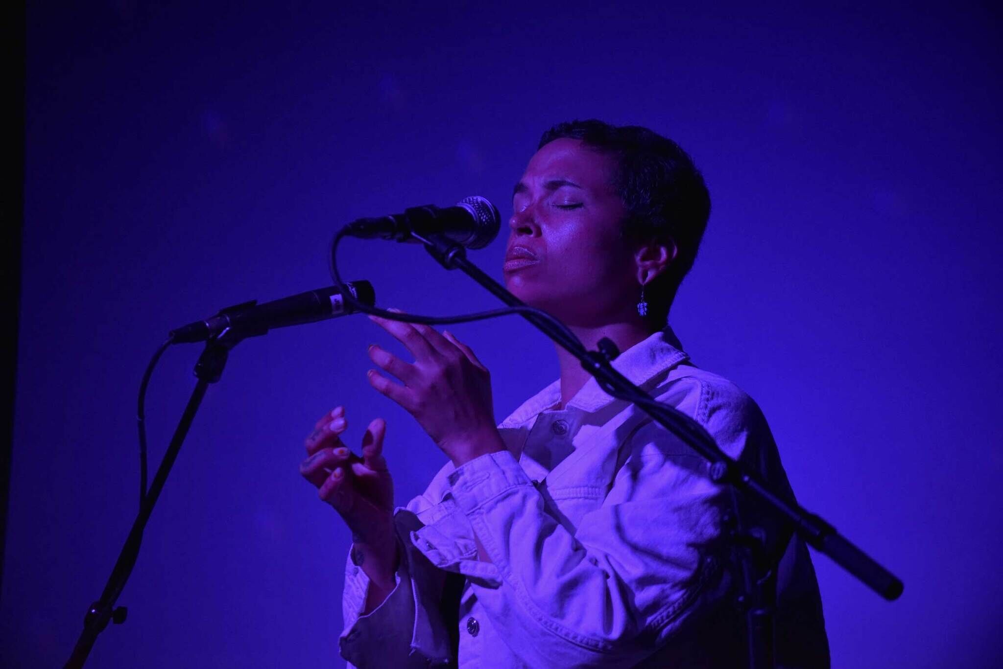 A singer performing on stage, bathed in blue light, eyes closed with emotion.