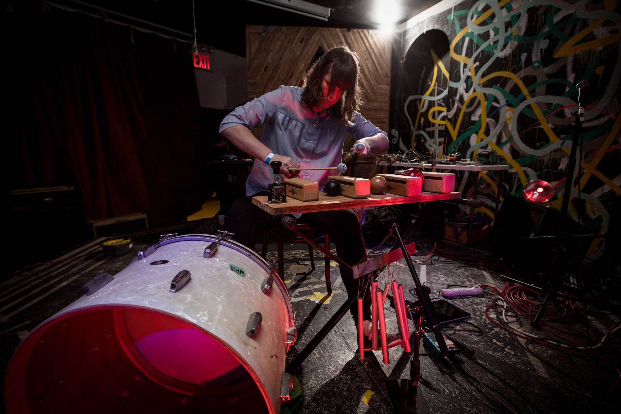A person playing an experimental music setup with various objects on a table, in front of a colorful graffiti backdrop.