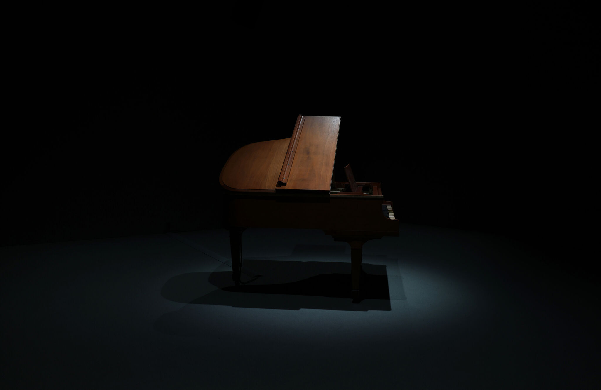 A grand piano illuminated by a single spotlight against a dark background.