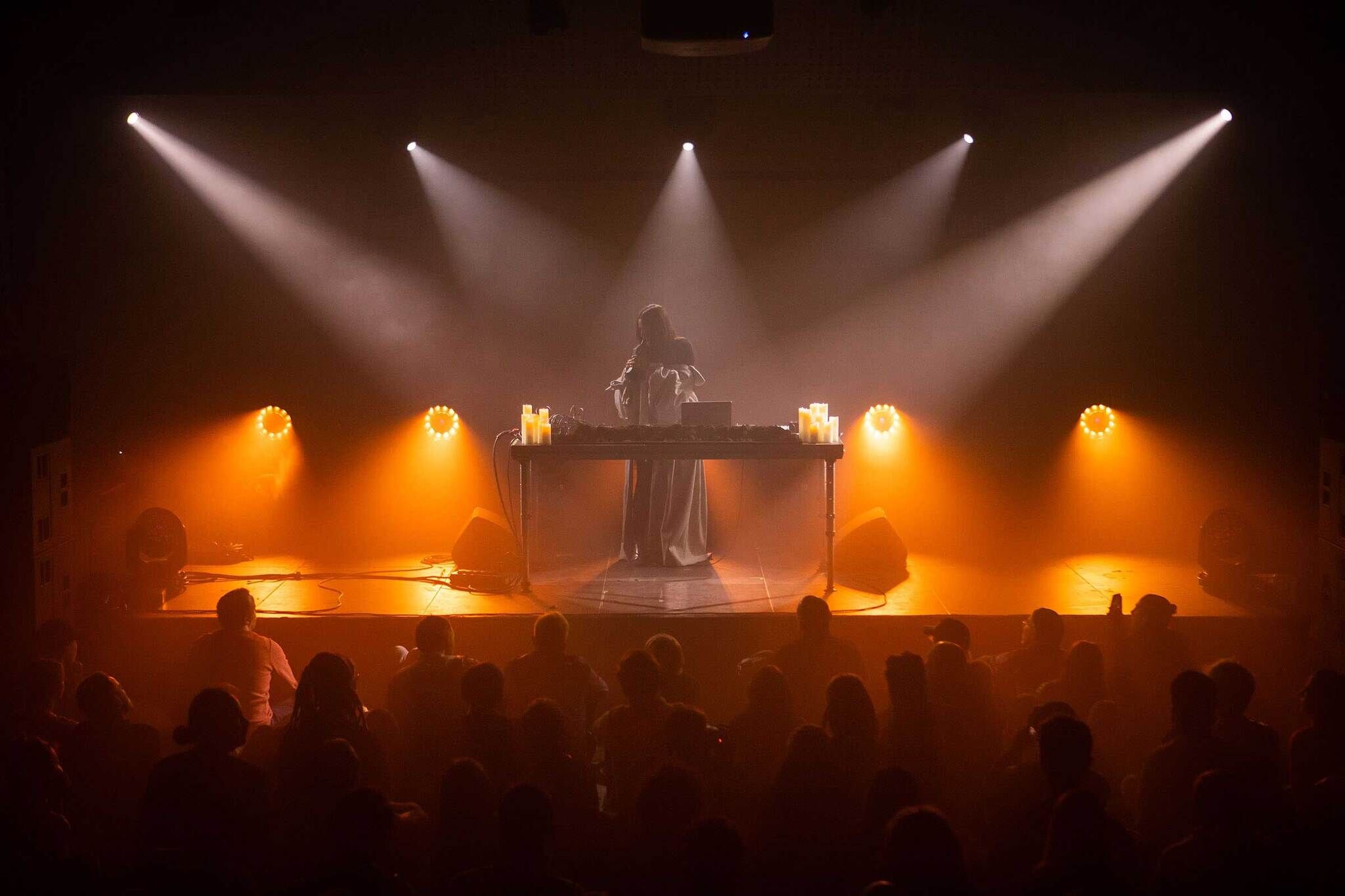 DJ performs on stage with atmospheric lighting as an audience watches.