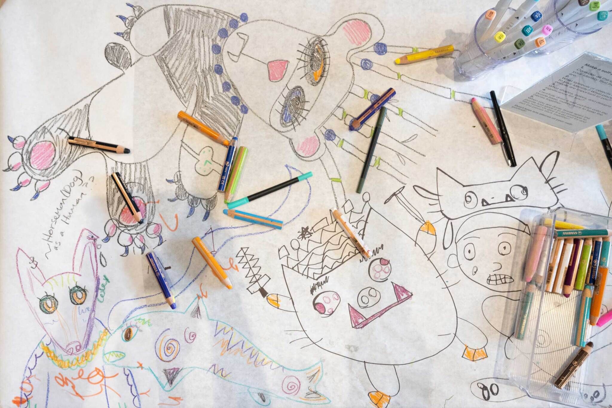 White butcher paper filled with doodles of colorful animals. Markers are splayed across the surface. 