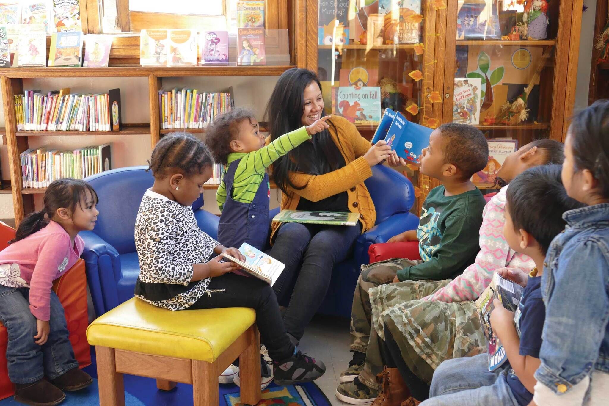 A librarian sits in the middle of a group of young children, reading a book. 
