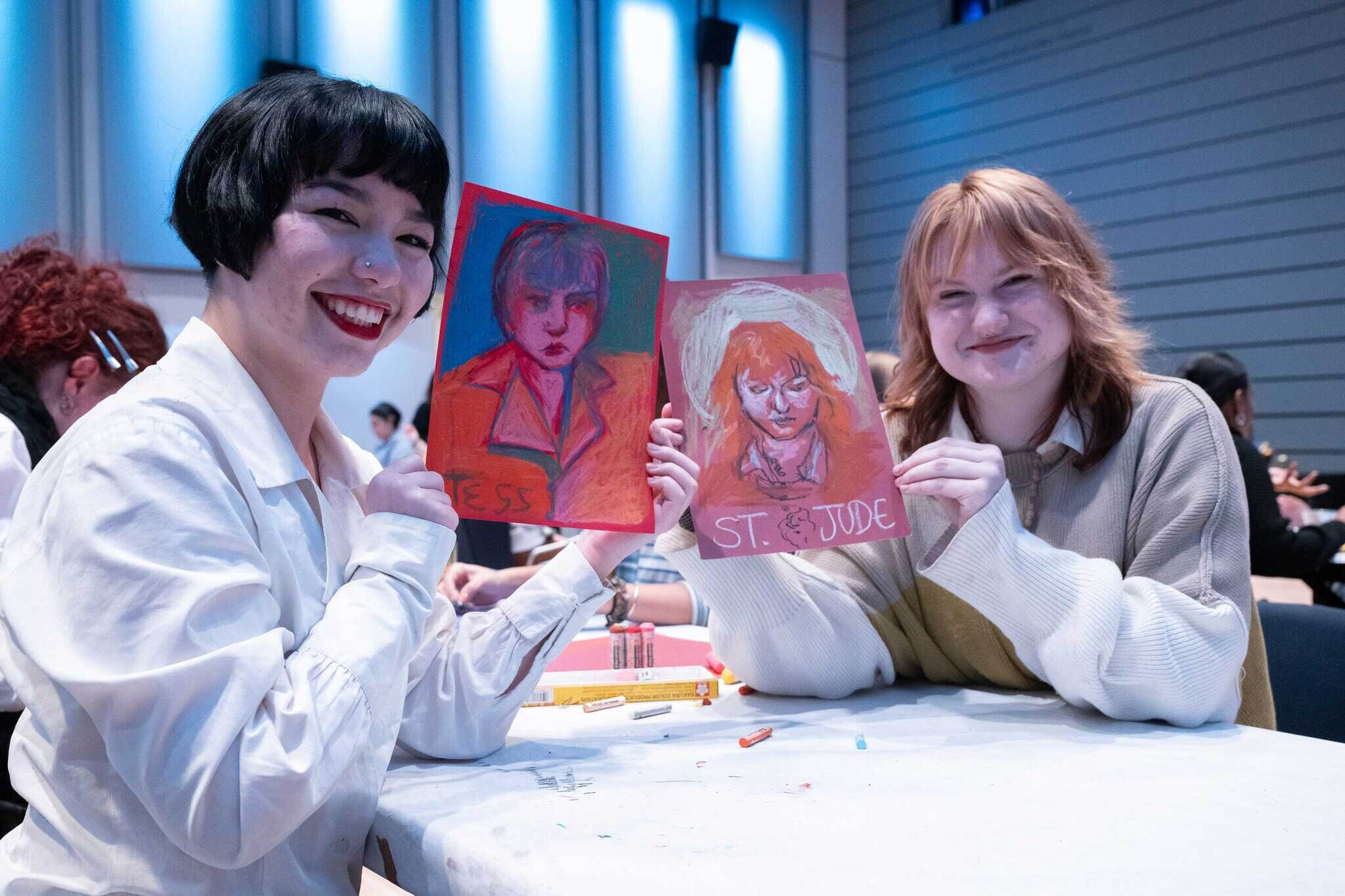 Two smiling people holding up colorful portrait drawings.