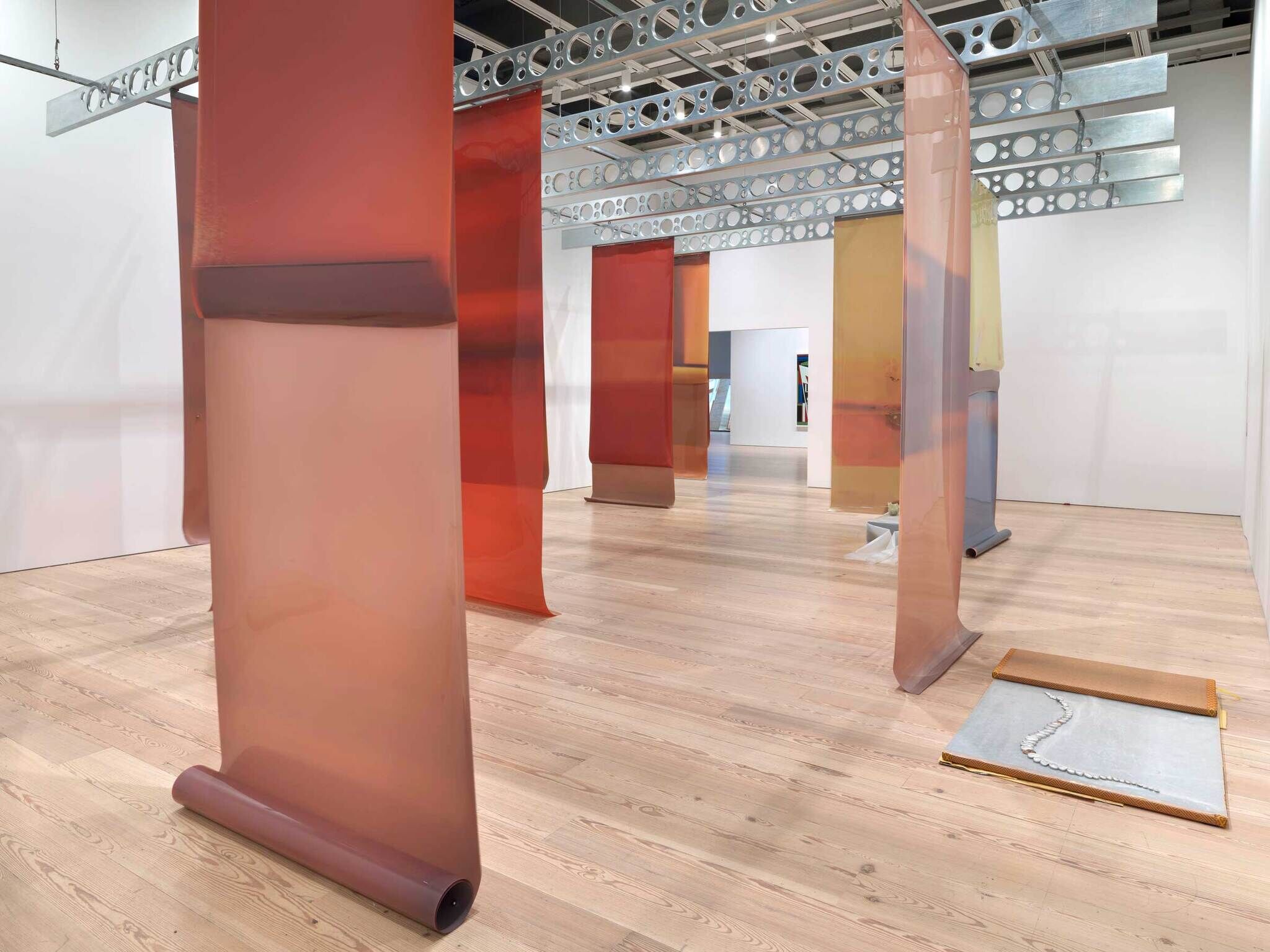 Modern art installation with translucent red film panels in a gallery with wooden floors and industrial ceiling.