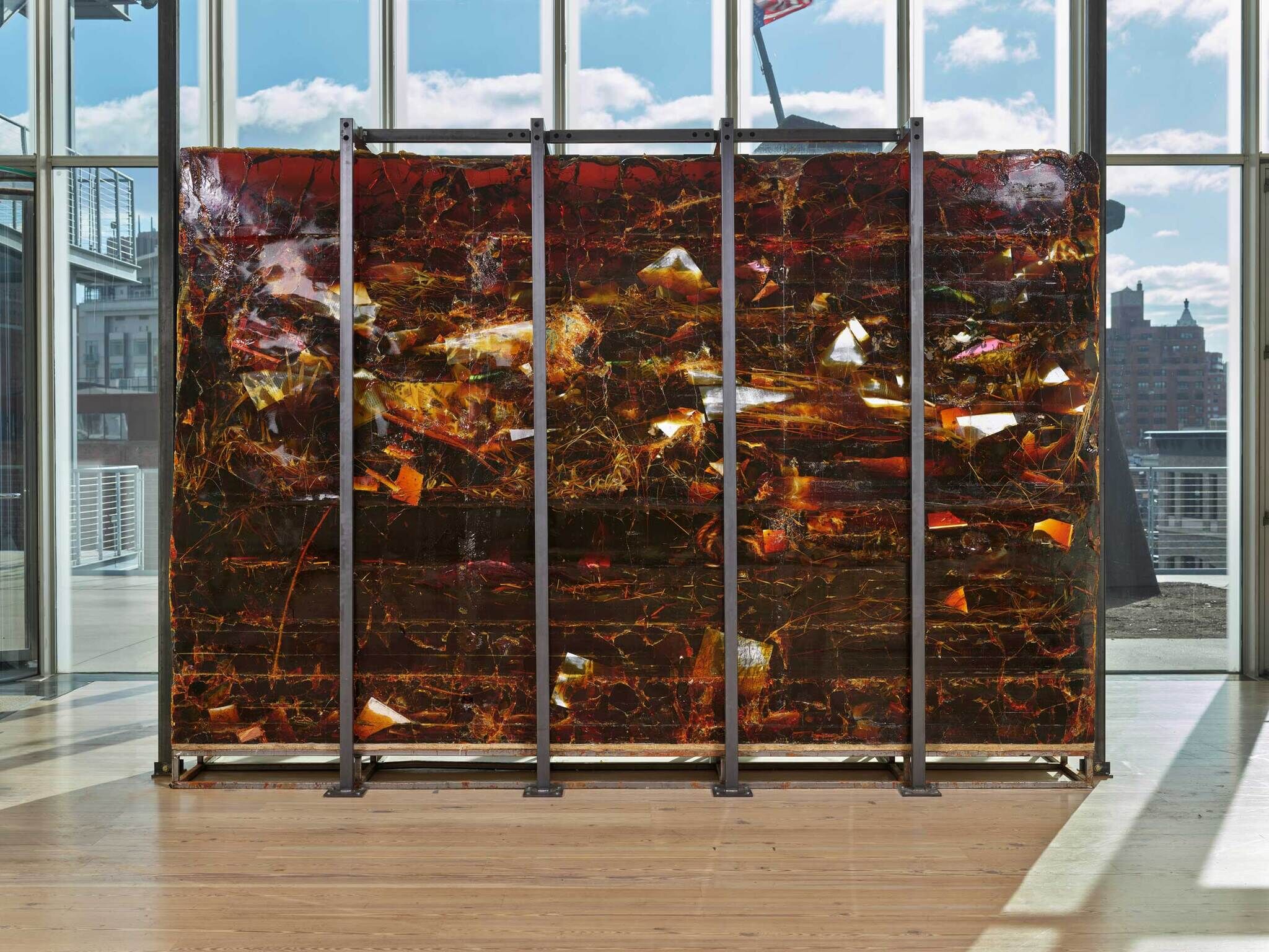 Large translucent art installation with amber hues in a room with floor-to-ceiling windows and cityscape views.