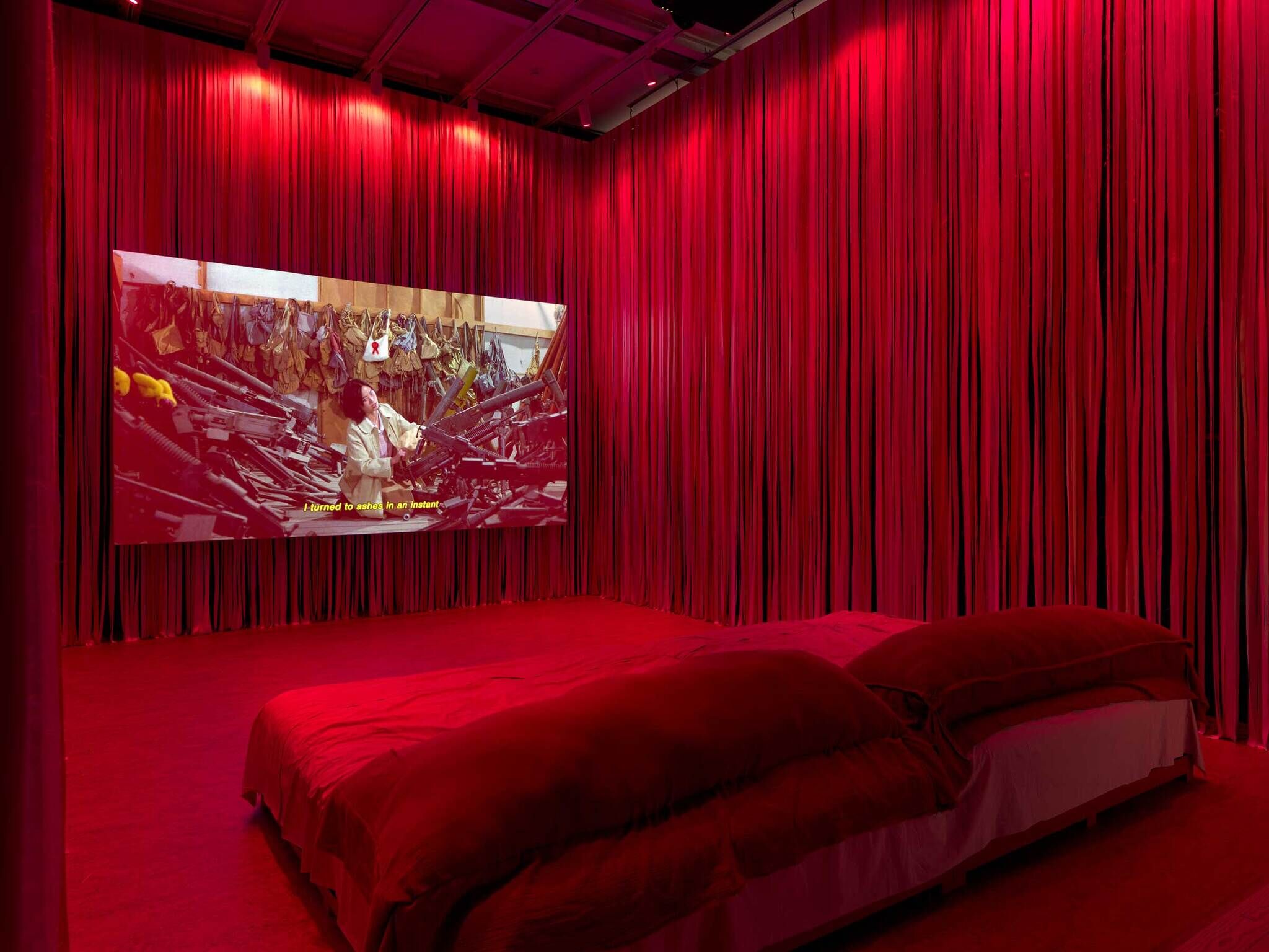 A red-themed room with curtains, a large bed, and a screen displaying a dramatic scene with the text "Turned to ashes in an instant."