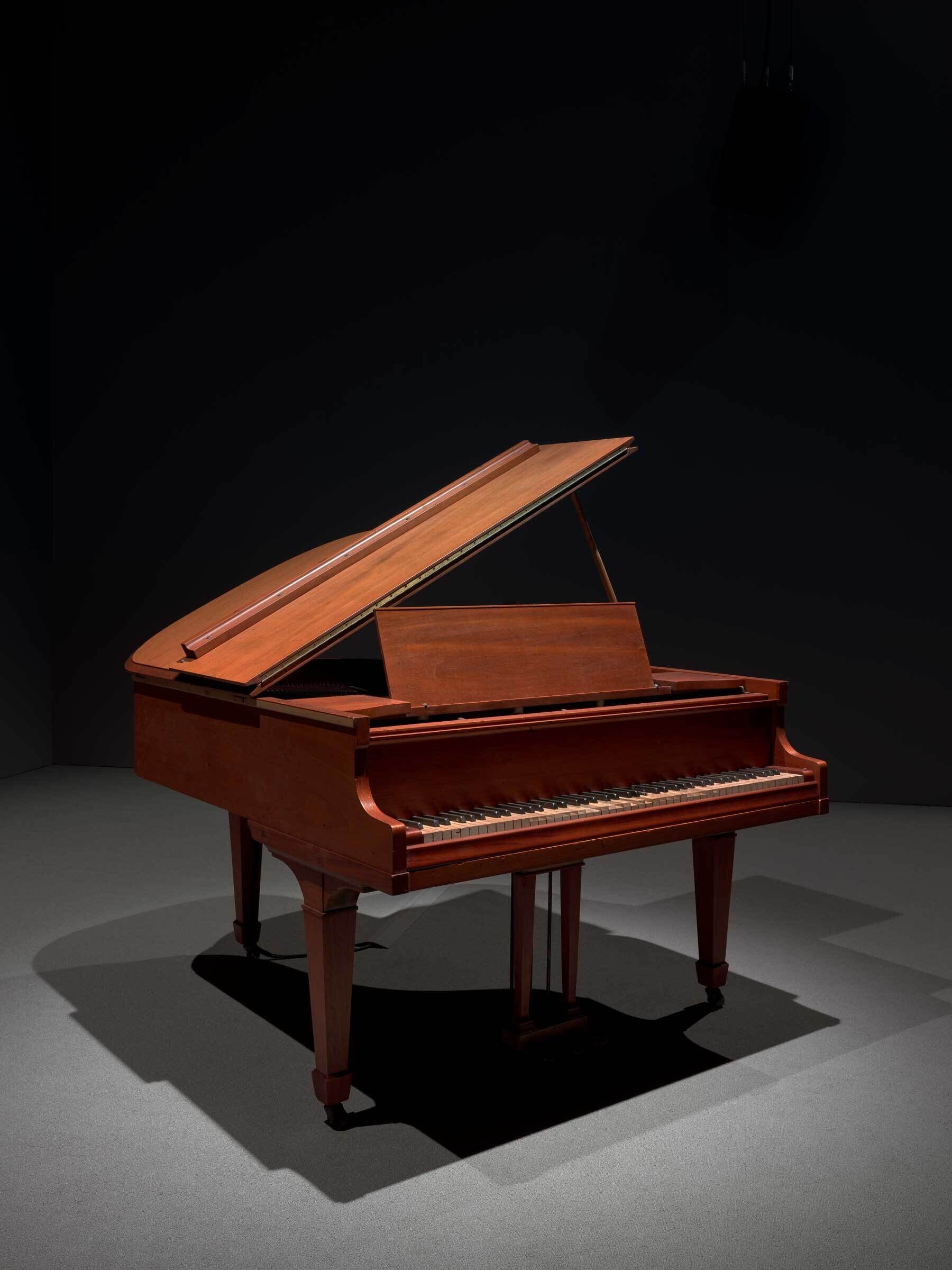 A grand piano with its lid open, set against a dark background with soft lighting.