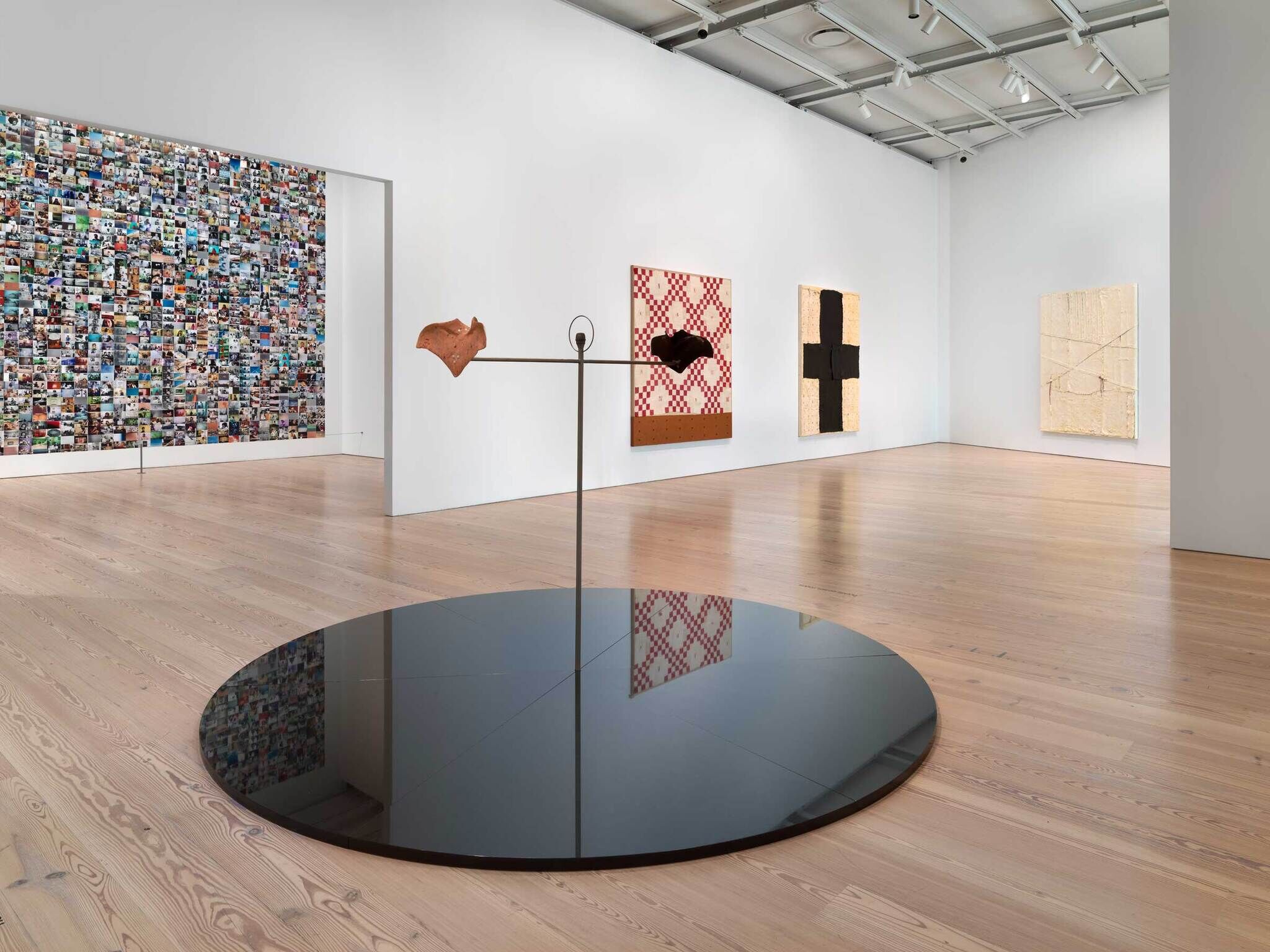 Modern art gallery interior with various abstract artworks on walls and a sculpture with a reflective base on the floor.