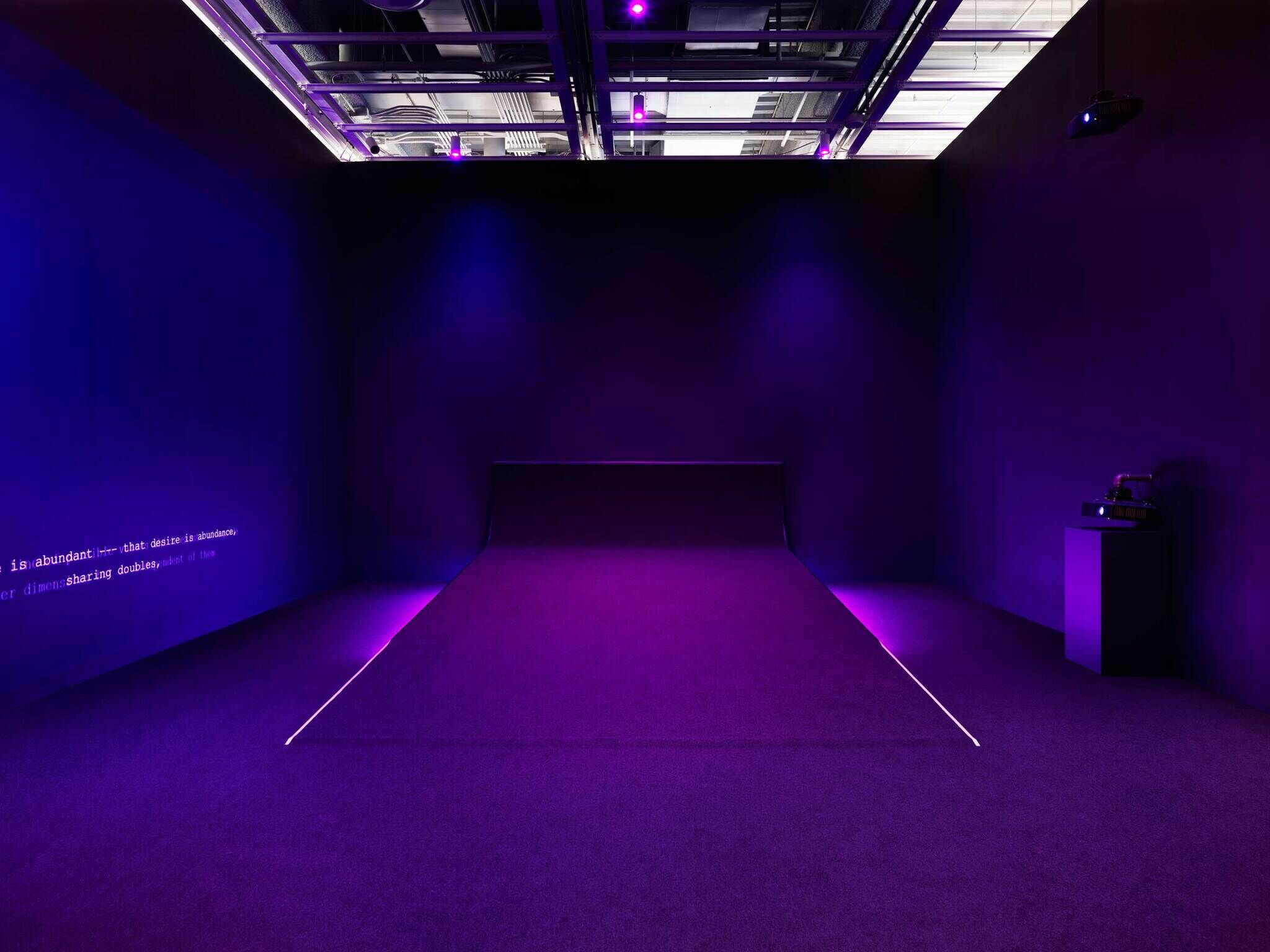 A dimly lit room with purple lighting, featuring a minimalist art installation with a neon line on the floor.