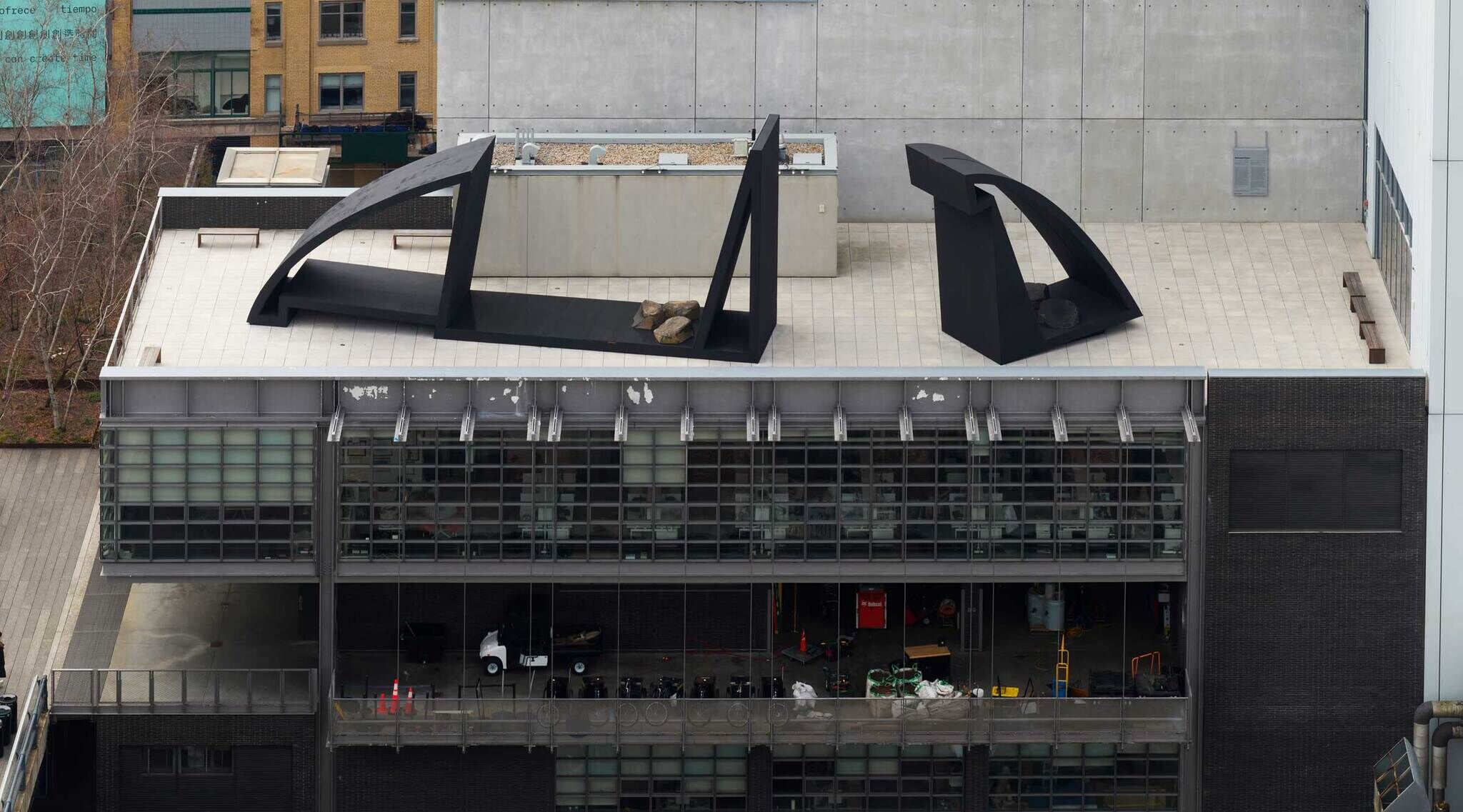 Aerial view of a building rooftop with two large, abstract black sculptures and a glimpse into the interior floors below.