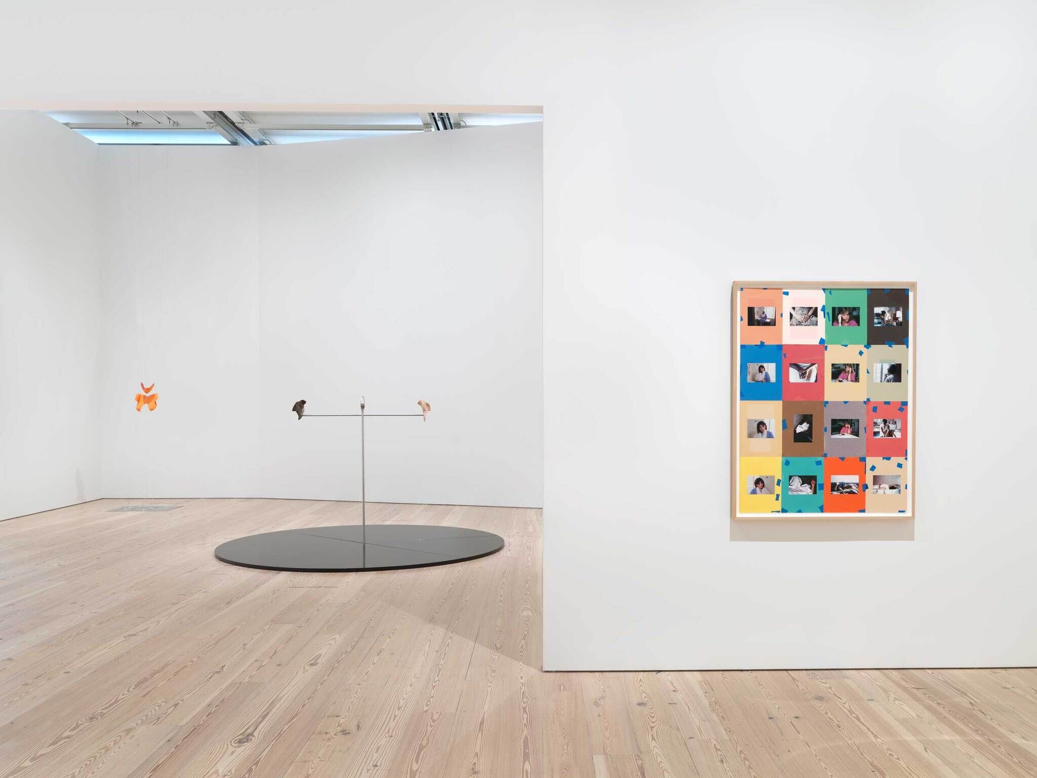 Minimalist art gallery interior with a circular sculpture, two wall-mounted pieces, and a collage of images on the right.