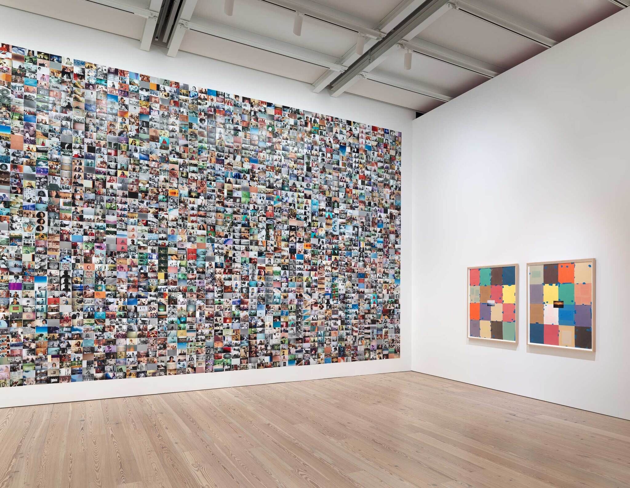 A gallery wall covered in a dense collage of varied photos with two abstract paintings to the right.