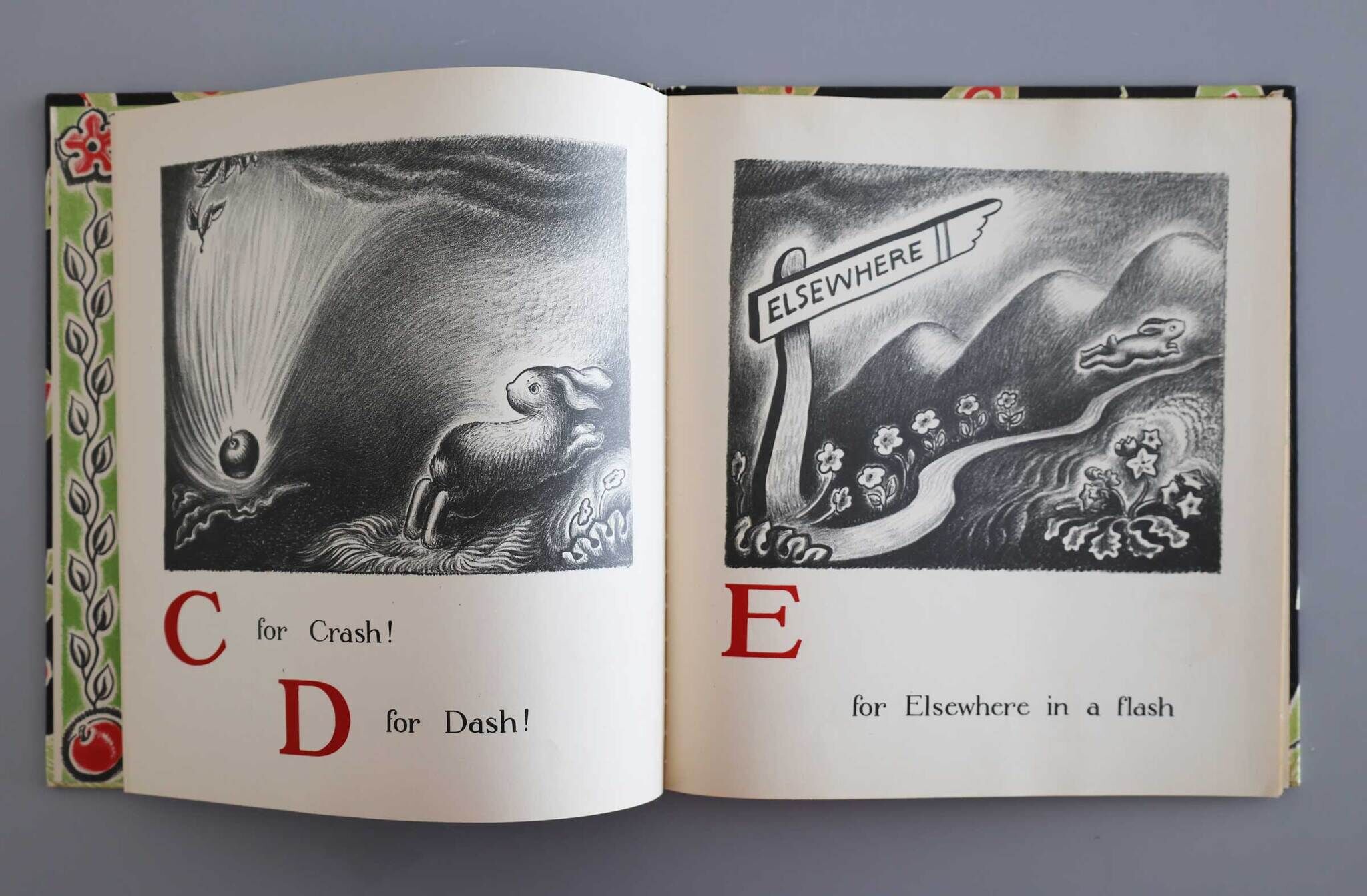 Open book with illustrated pages showing "C for Crash!" with a bowling ball and "D for Dash!" with a rabbit by a sign "ELSEWHERE."