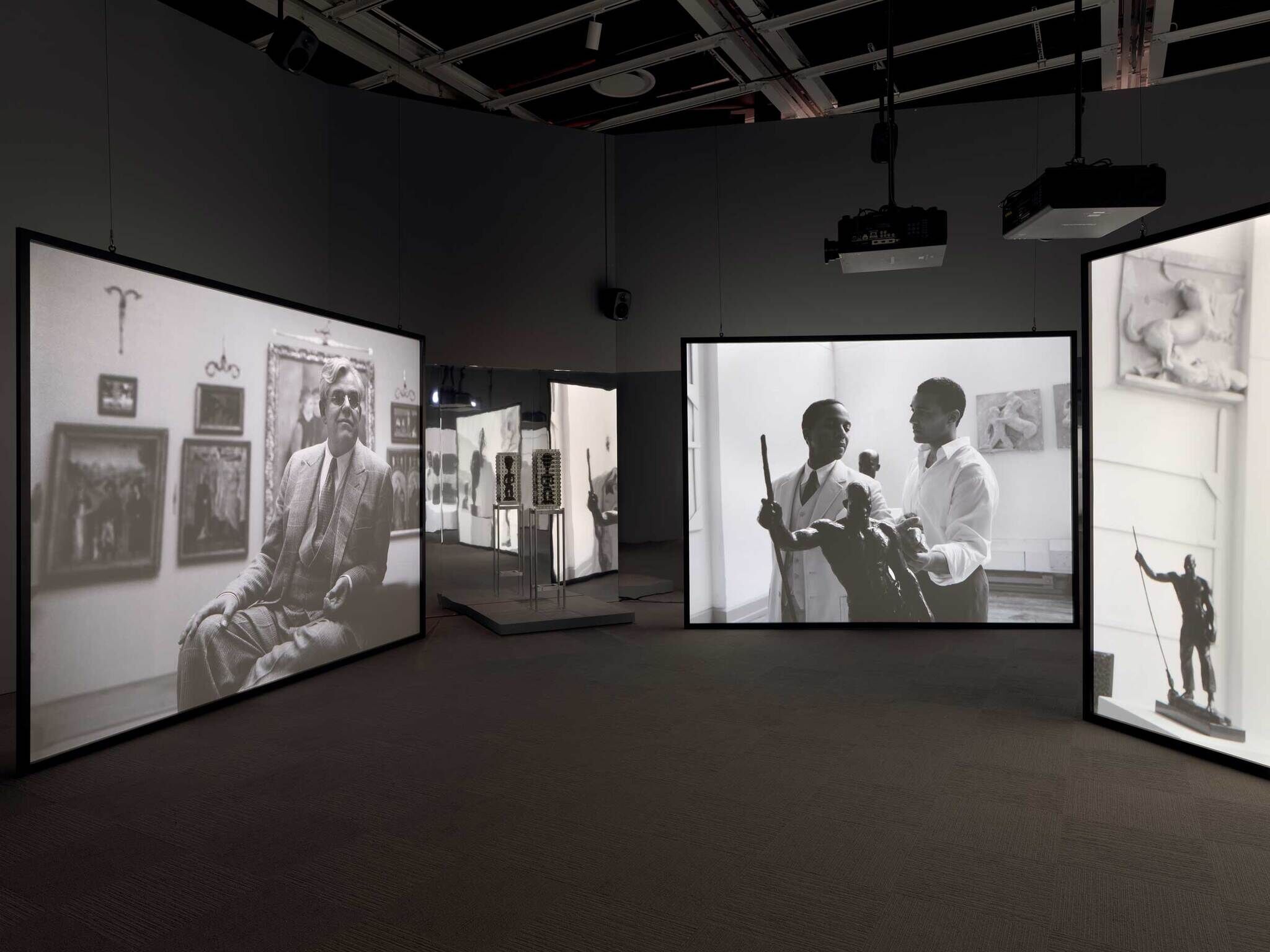 Art exhibition with large monochrome photographs displayed on screens in a dimly lit room.