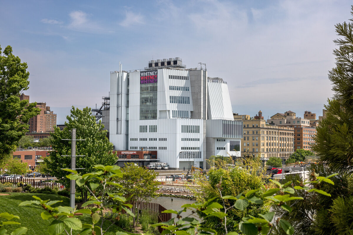 Modern museum building with staggered white facade, surrounded by greenery and urban backdrop.