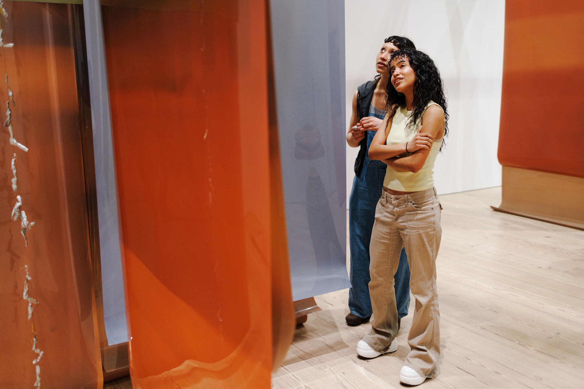 Two people stand in an art gallery, observing large hanging orange and blue panels.
