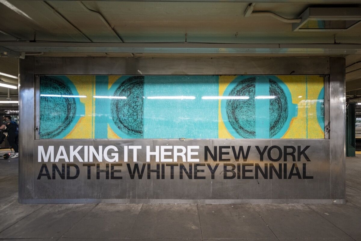 Subway station mural with text "MAKING IT HERE NEW YORK AND THE WHITNEY BIENNIAL" in bold letters, featuring abstract circular designs.