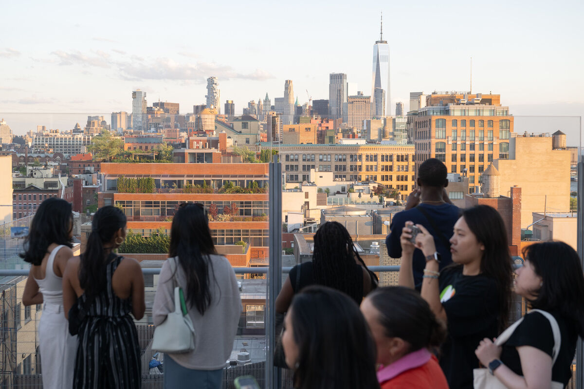 People on a rooftop terrace in New York City, taking photos and enjoying the view of the skyline, including the One World Trade Center.