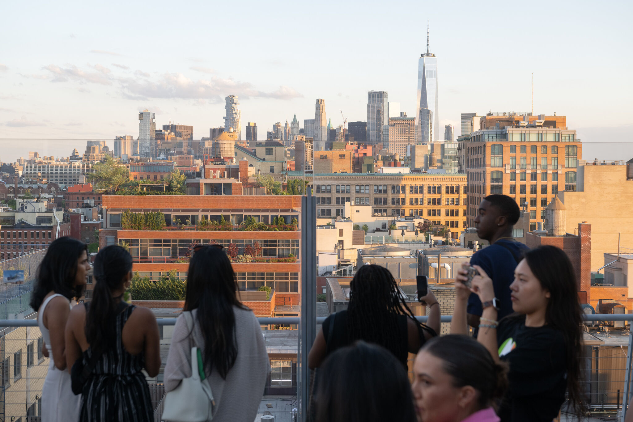 People on a rooftop terrace admire a cityscape with modern and historic buildings, including a tall skyscraper in the background.