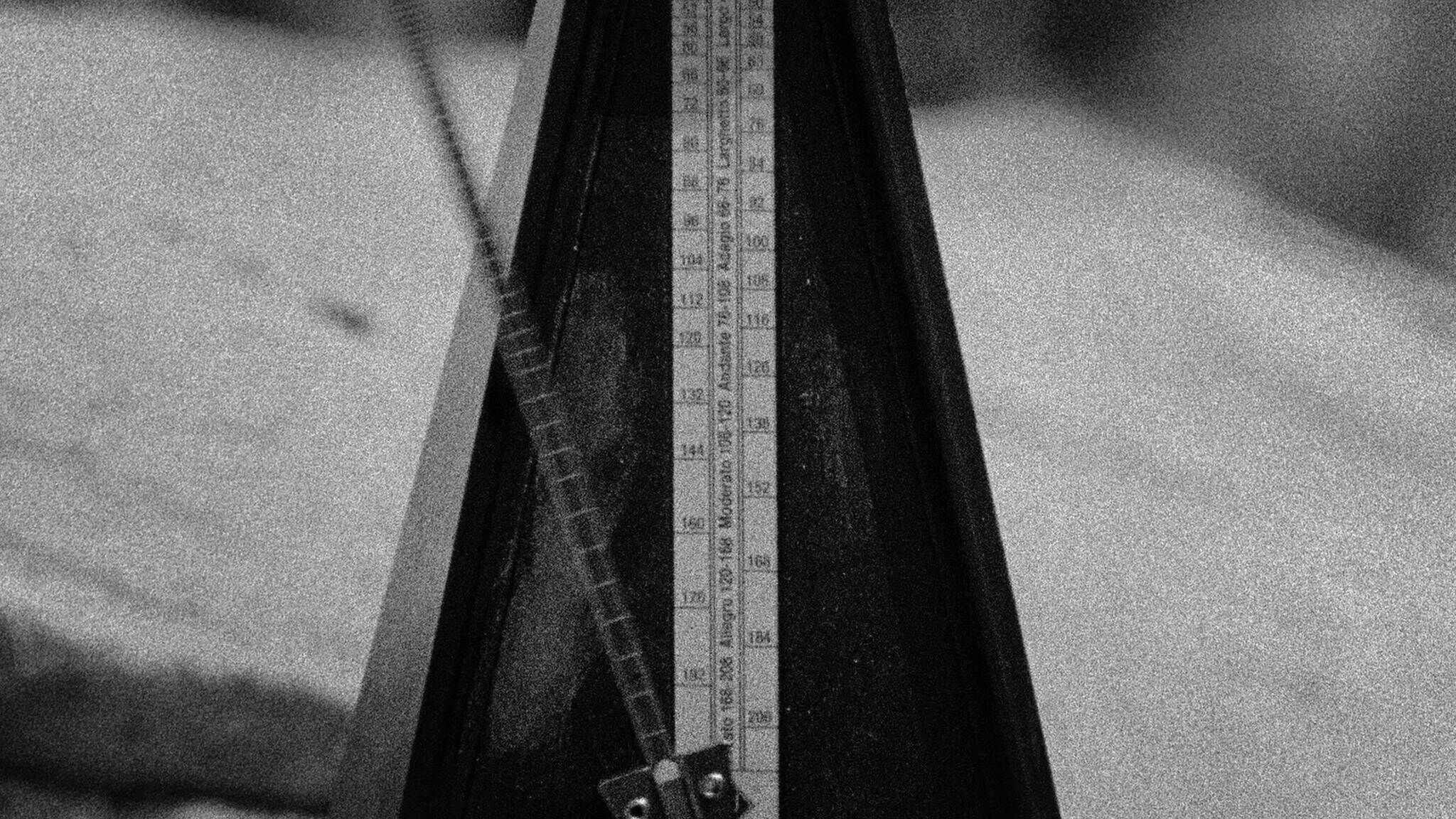 A black and white image of a metronome with its pendulum in motion, showing tempo markings on the front scale.